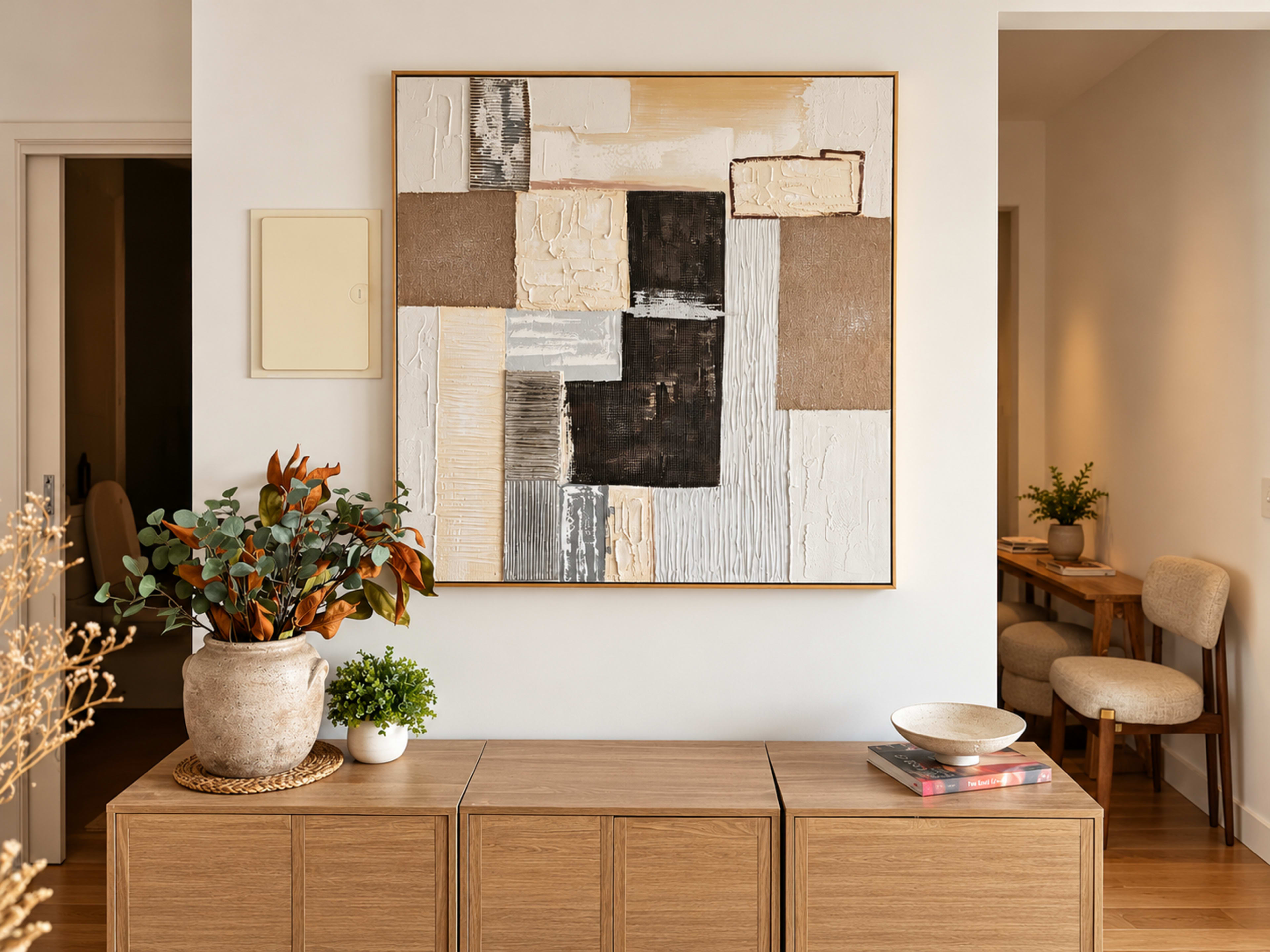 The image features a modern interior space with a wooden sideboard displaying a decorative bowl and books, complemented by a large abstract artwork on the wall above it.