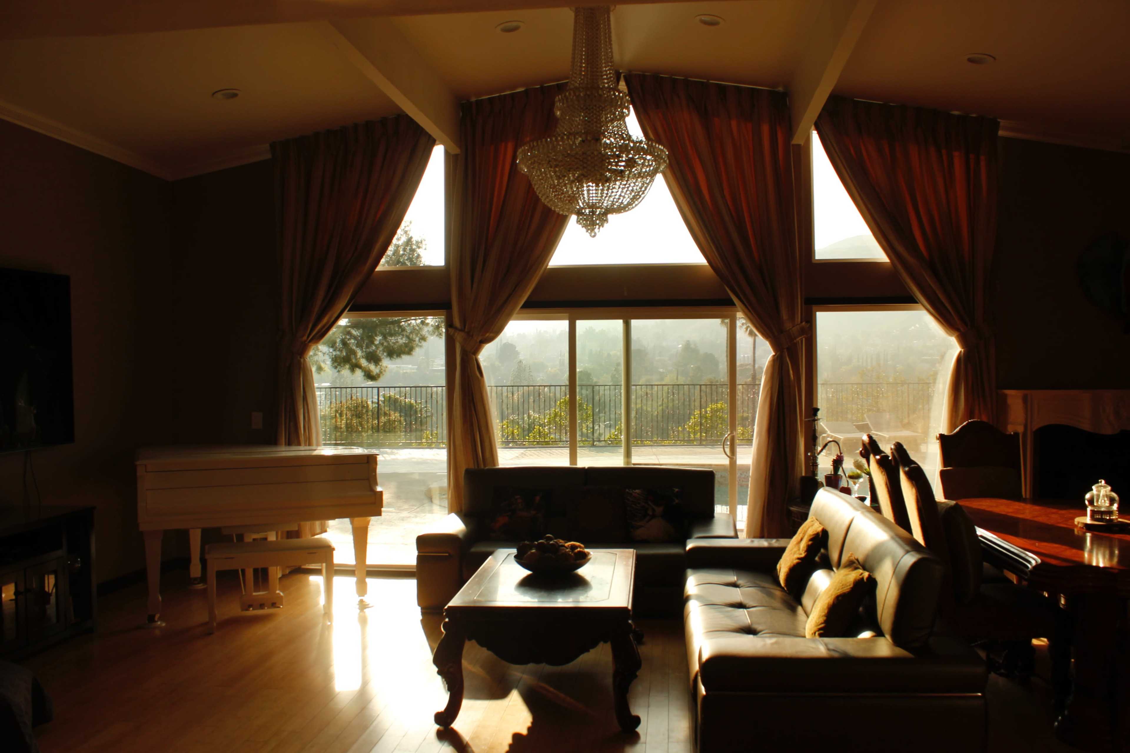 A spacious living room features a grand piano, a coffee table, and large windows that overlook a scenic view, illuminated by soft natural light.