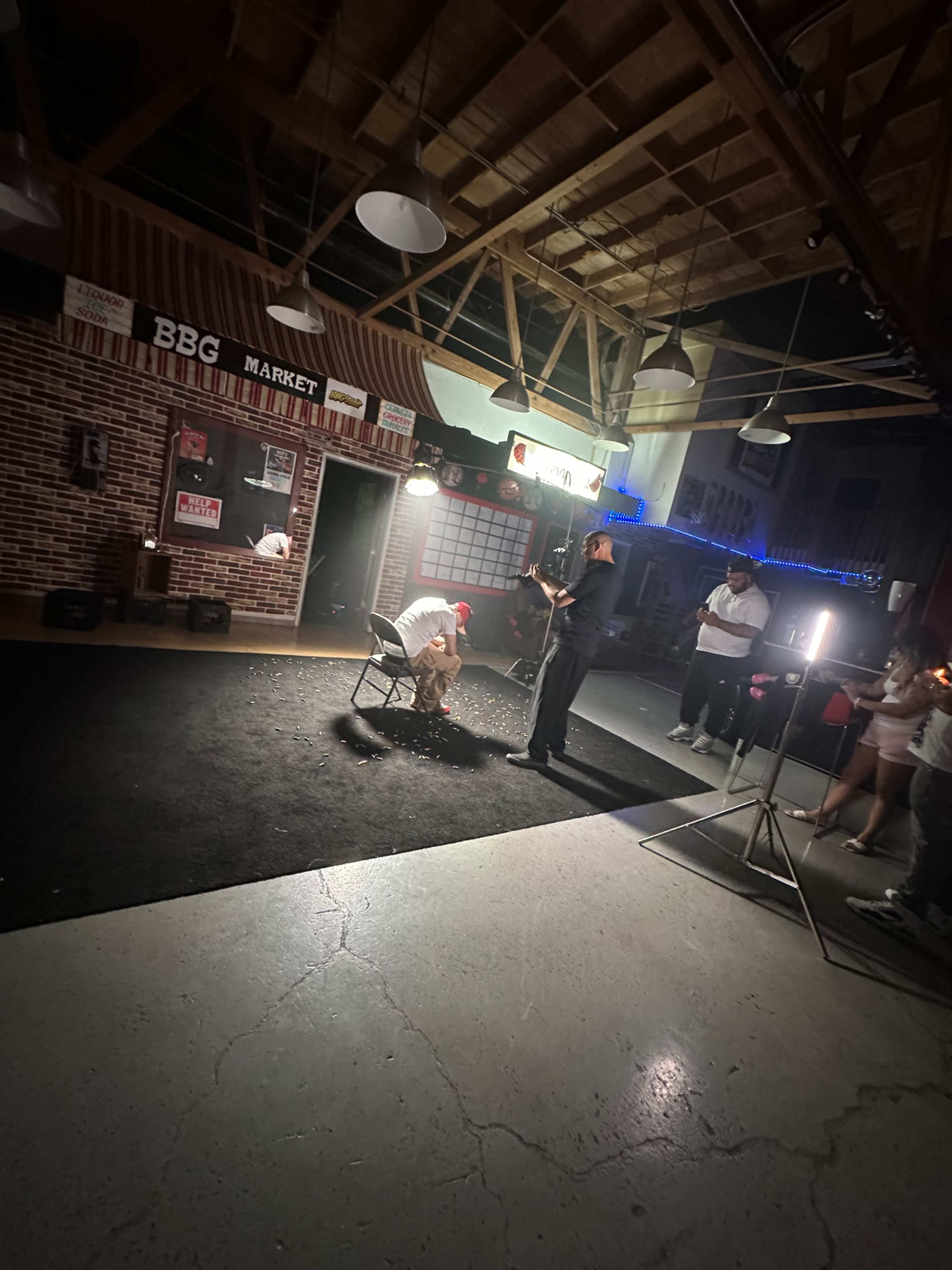A person in a white shirt sits on a chair in a dimly lit room while another person stands nearby holding a firework.