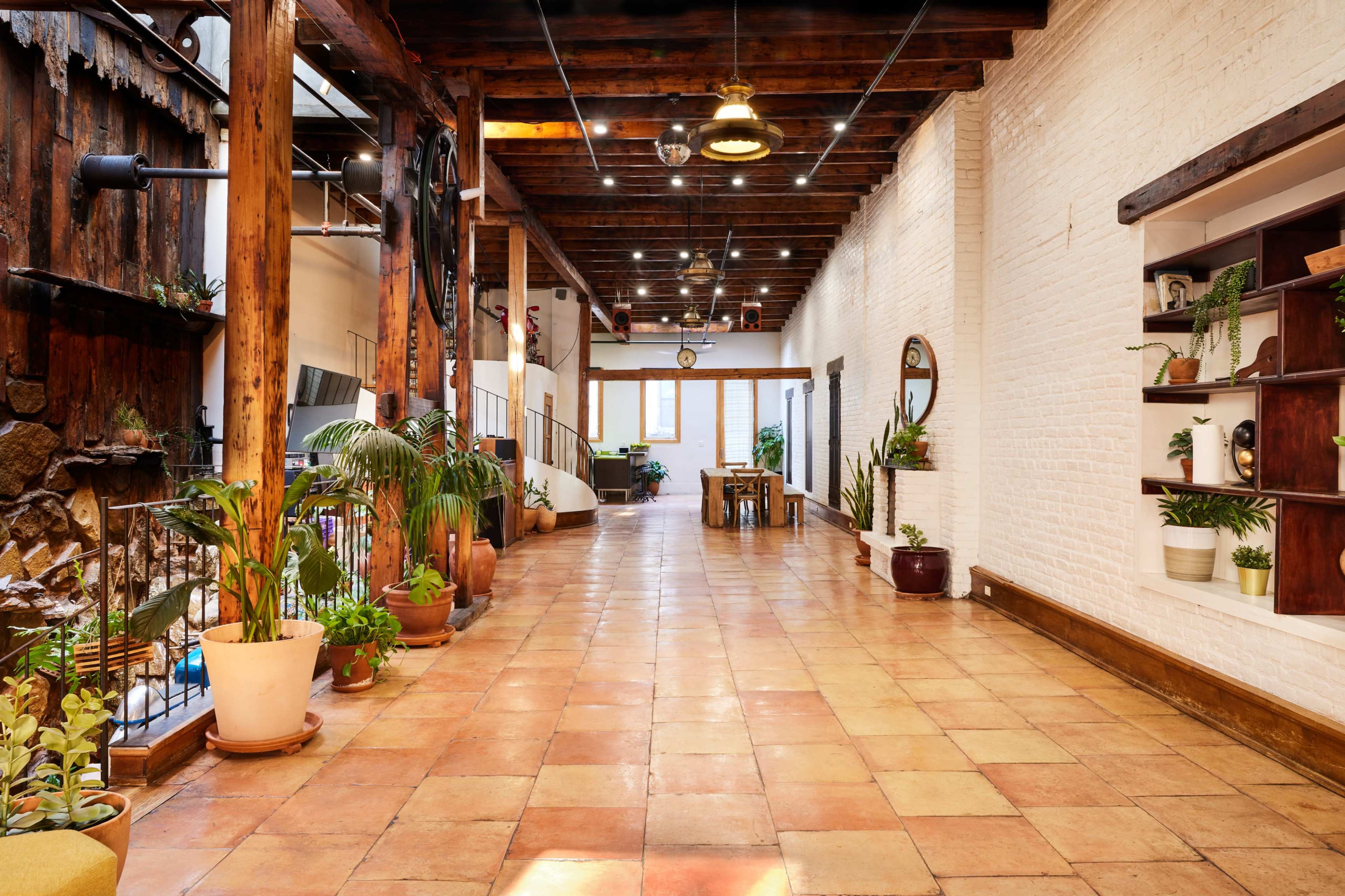 A spacious interior with a tiled floor, wooden beams overhead, and plants arranged along the walls.