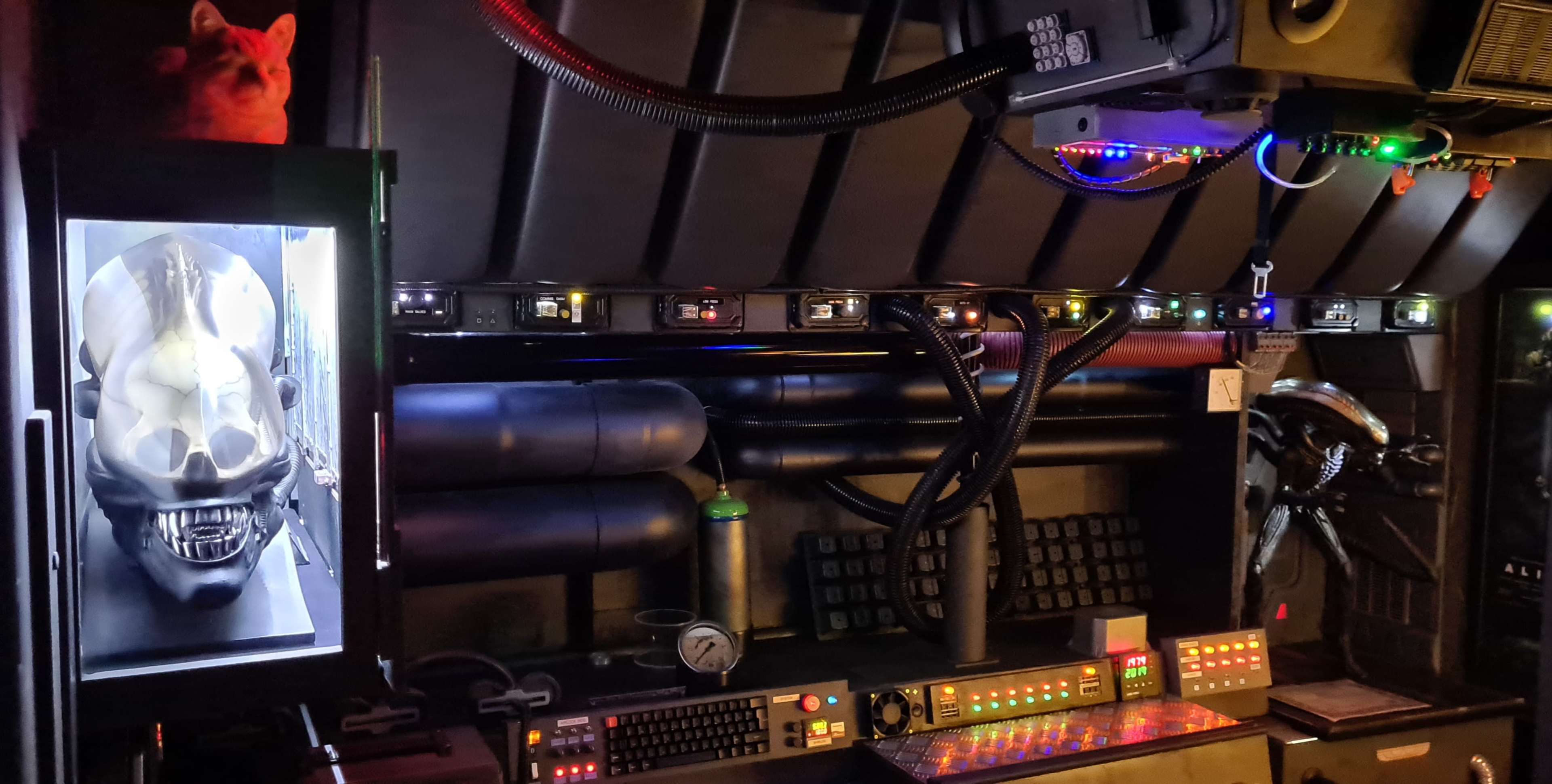 A dark, futuristic control room filled with various technological devices, a skull display, and a cat on a shelf.