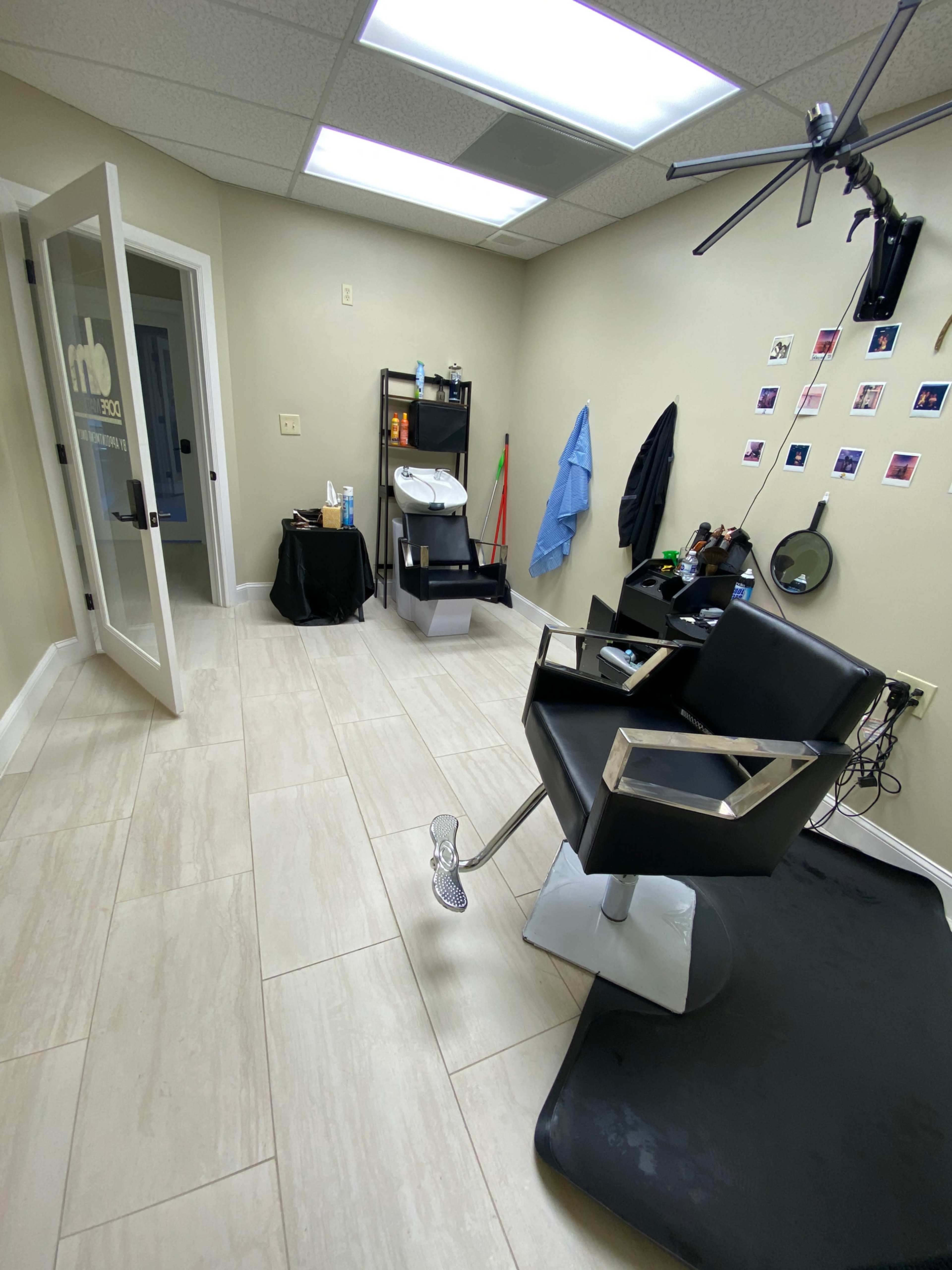 The image shows a neatly organized hair salon interior featuring a black salon chair, a shelf with various hair products, and a mirror against the wall.