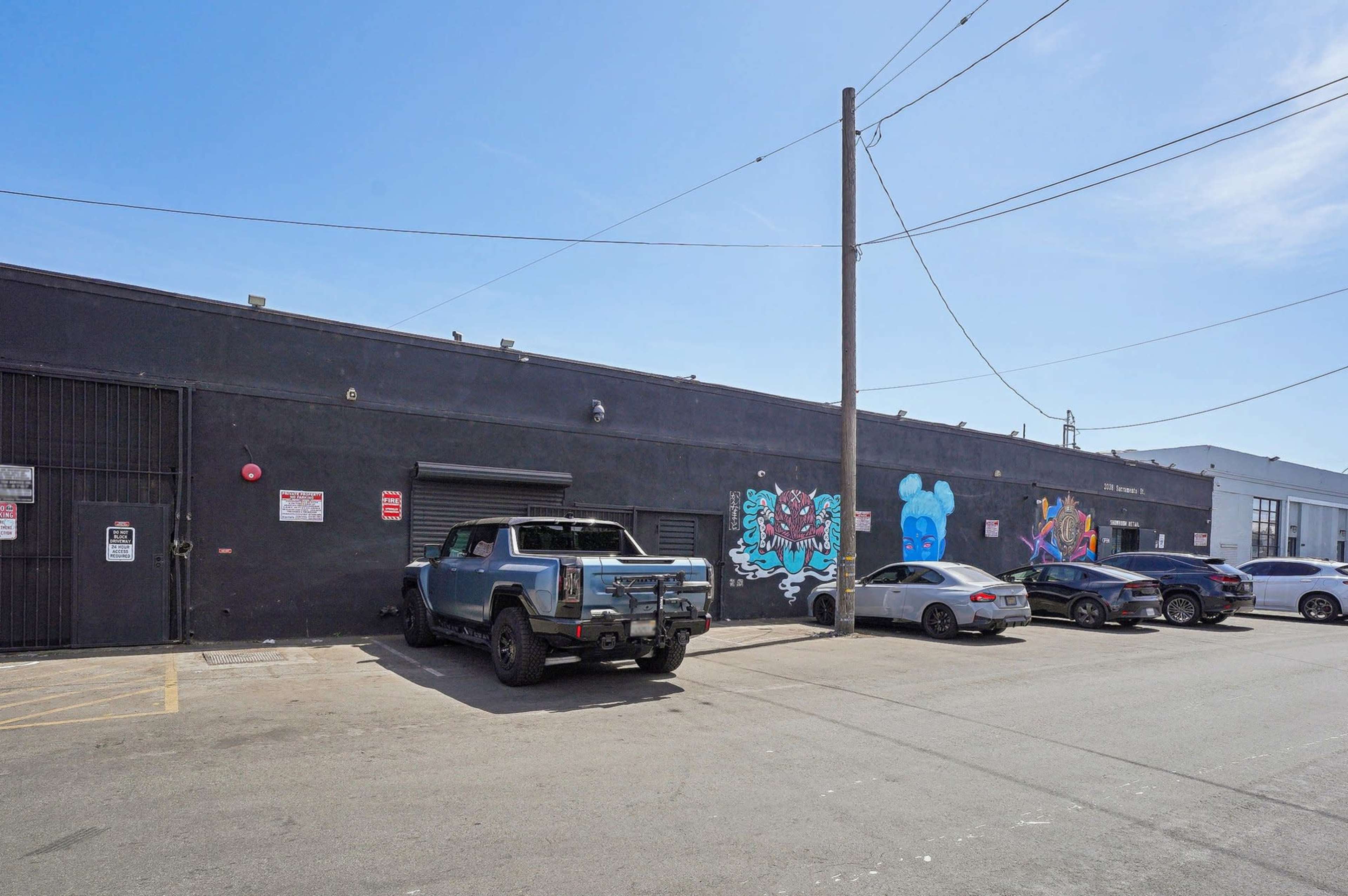 A blue pickup truck is parked next to a black building with a mural on the side, while several other cars are parked along the street.