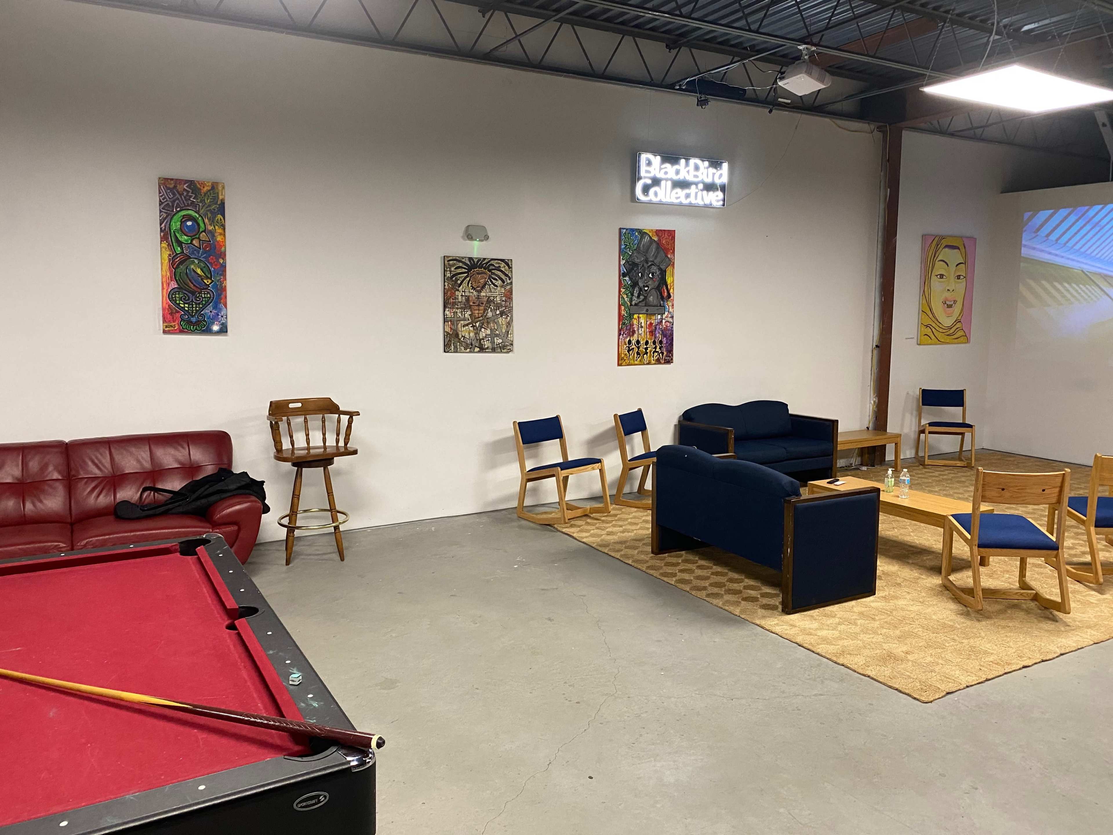 A communal room featuring a pool table, various chairs, a couch, and colorful wall art.
