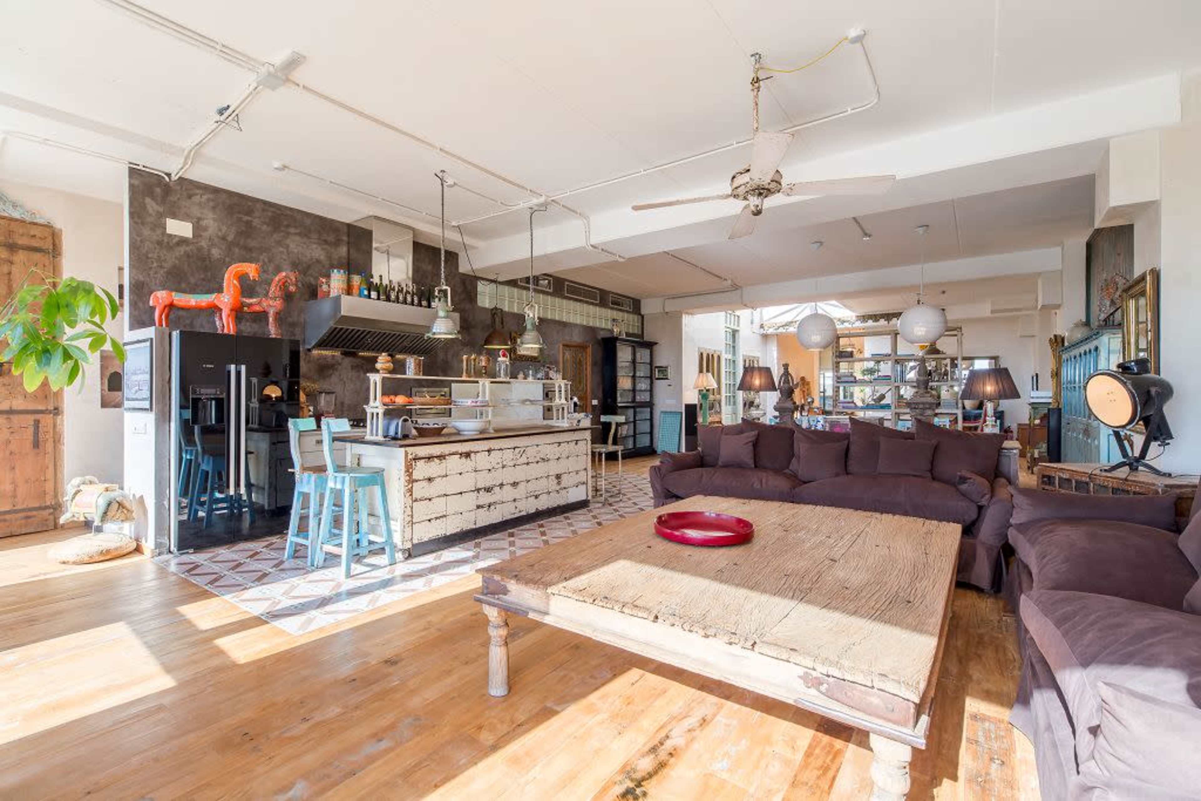 A spacious, modern open-concept living area with a large wooden table, a sectional sofa, and a well-equipped kitchen in the background.