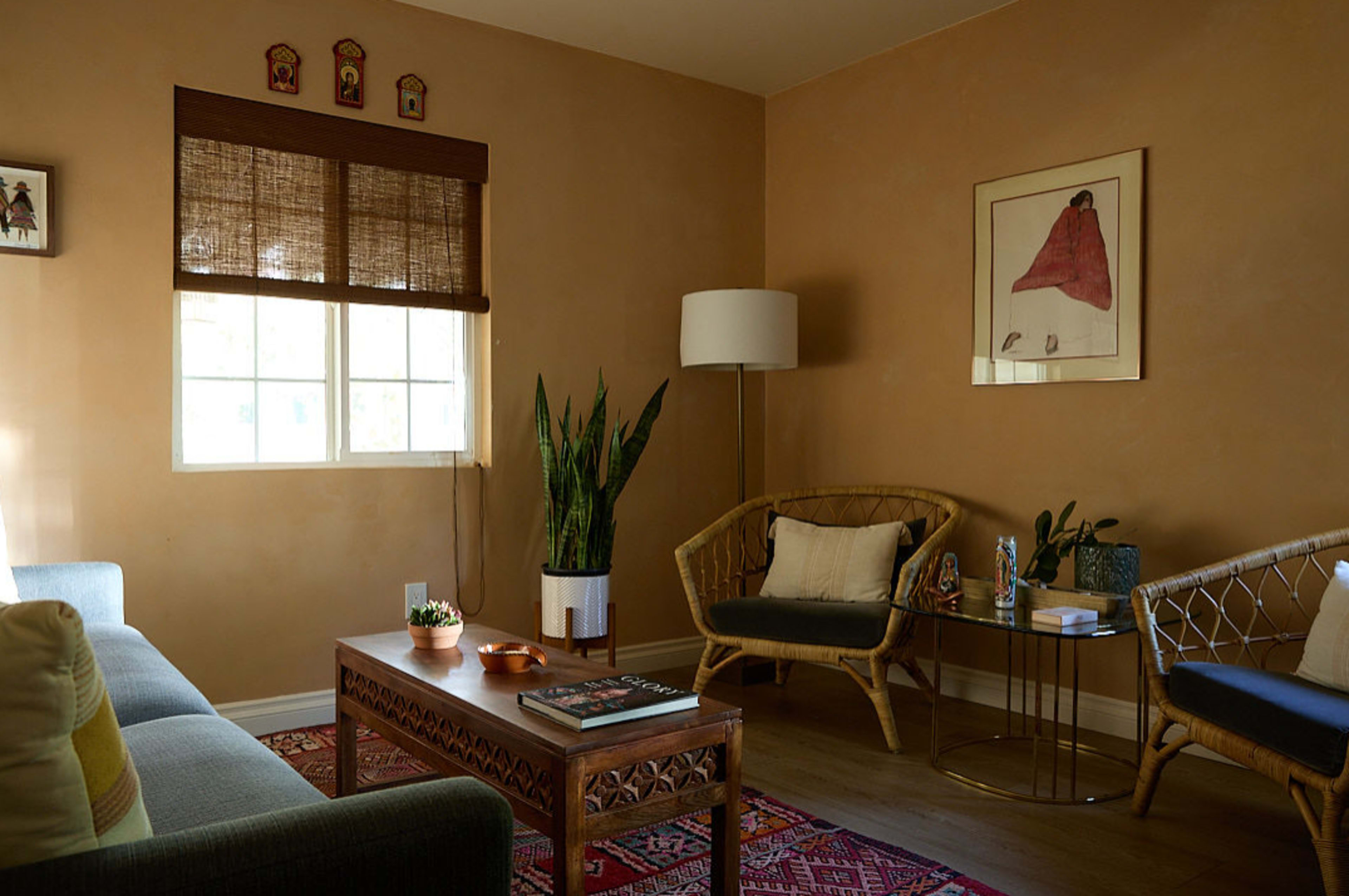 The image shows a cozy living room with beige walls, a wooden coffee table, and two seating areas, along with a window allowing natural light to enter.