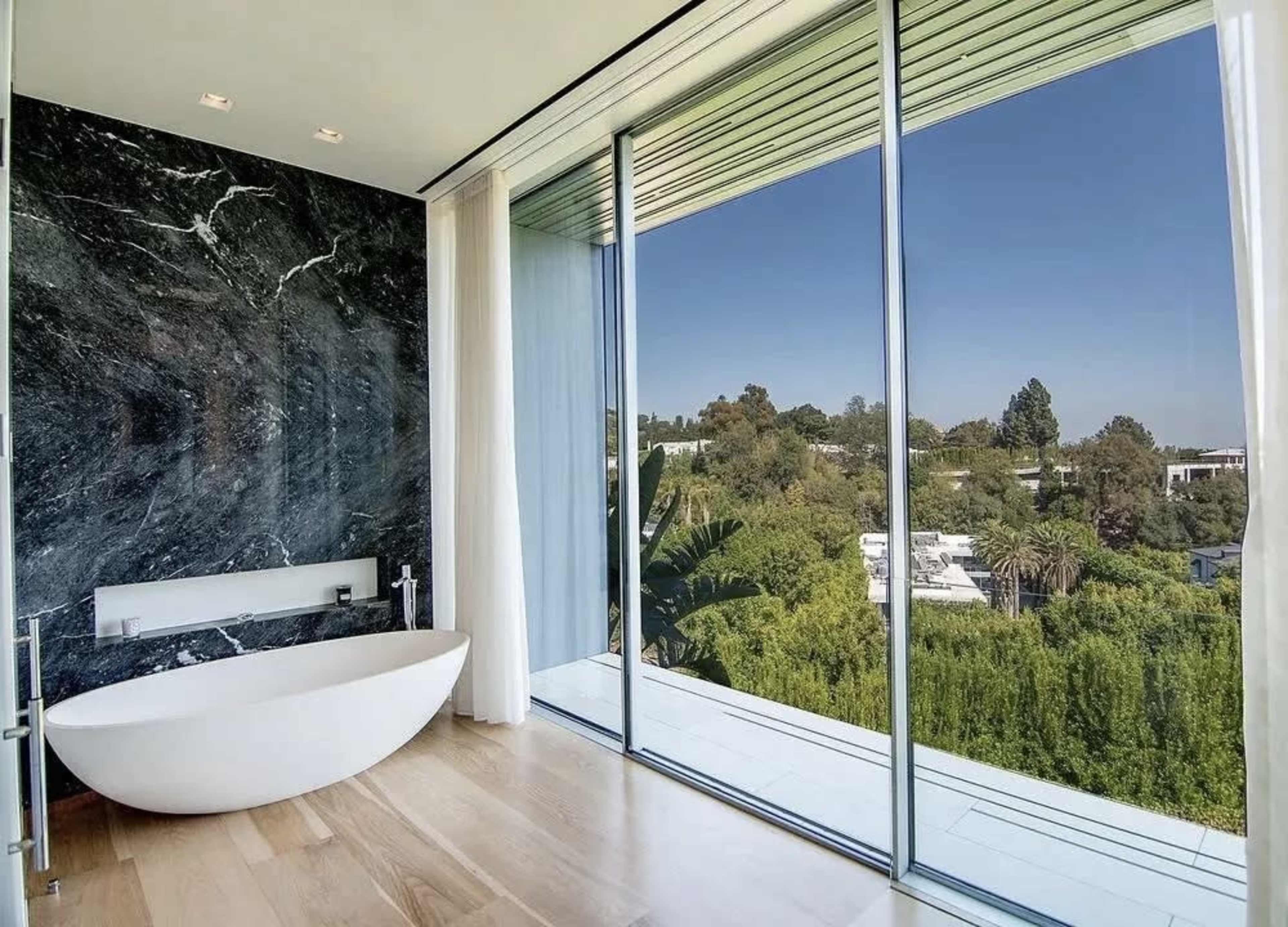 A modern bathroom featuring a freestanding bathtub and large glass windows that overlook a green landscape.
