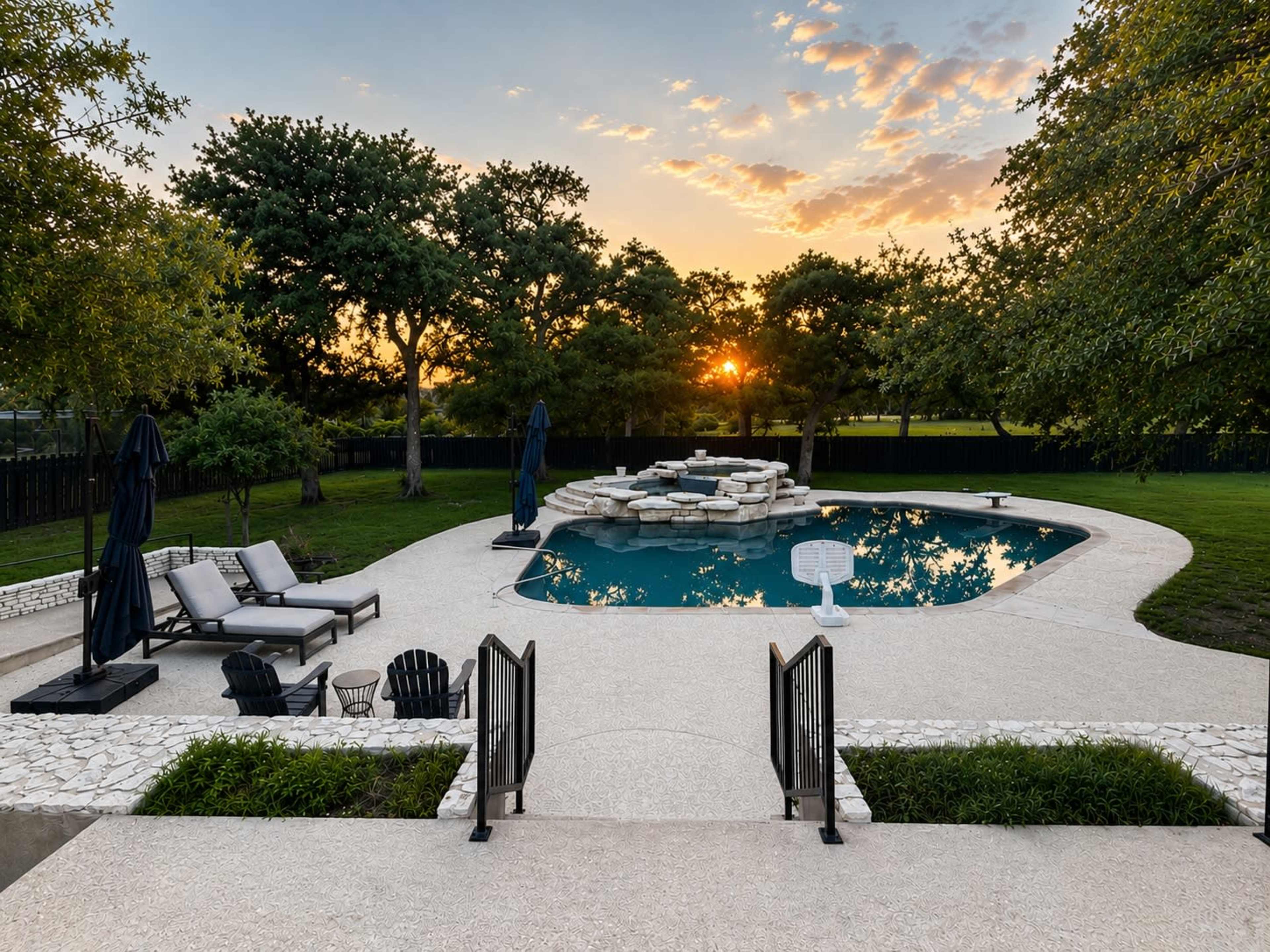 The scene depicts a backyard pool area with lounge chairs, a stone fountain, and trees, illuminated by a sunset sky.