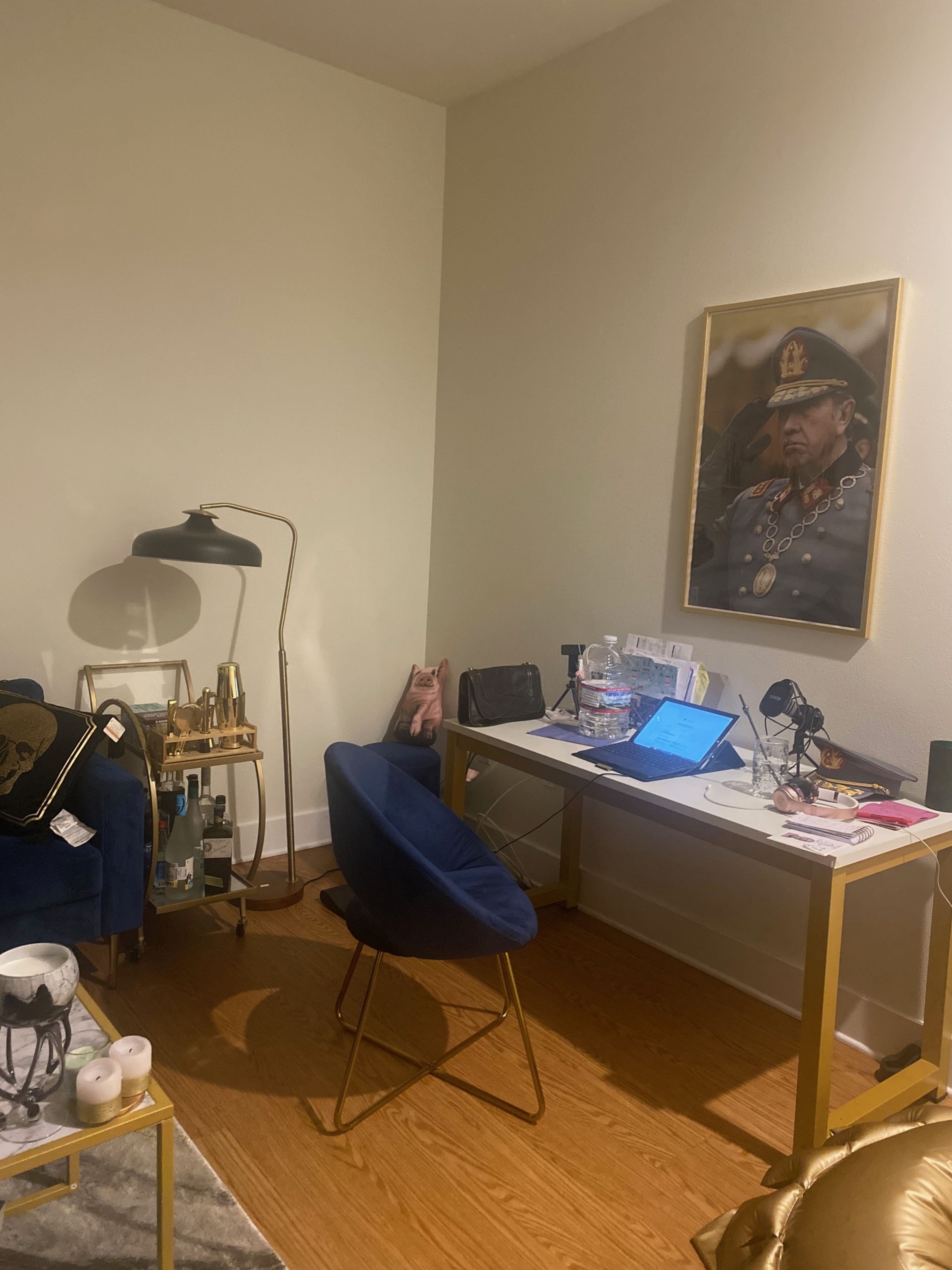The image shows a small office space with a desk, a chair, and a portrait of a man in a military uniform on the wall.
