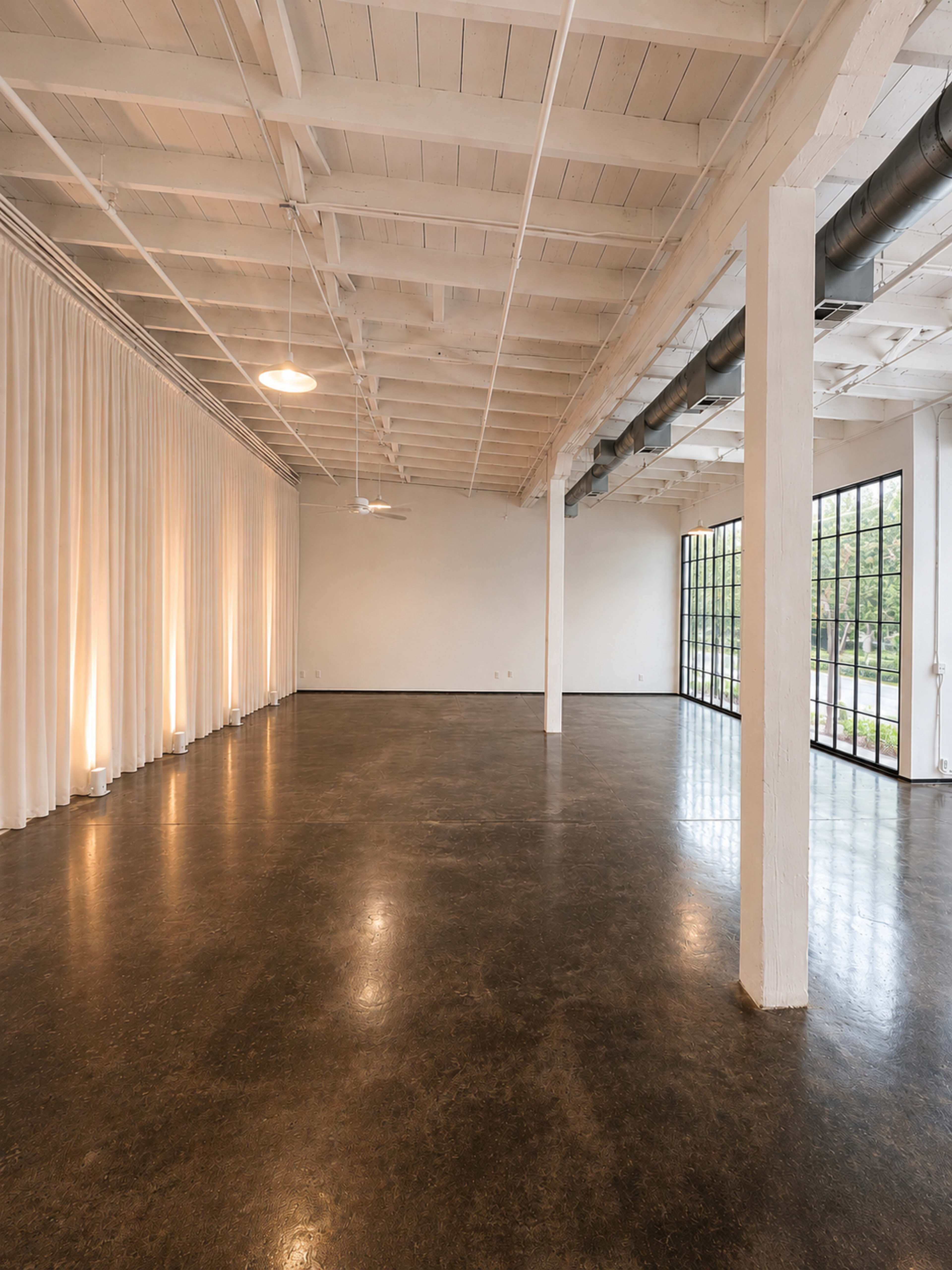 The image shows a spacious, empty room with high ceilings, large windows, and decorative curtains along one wall.