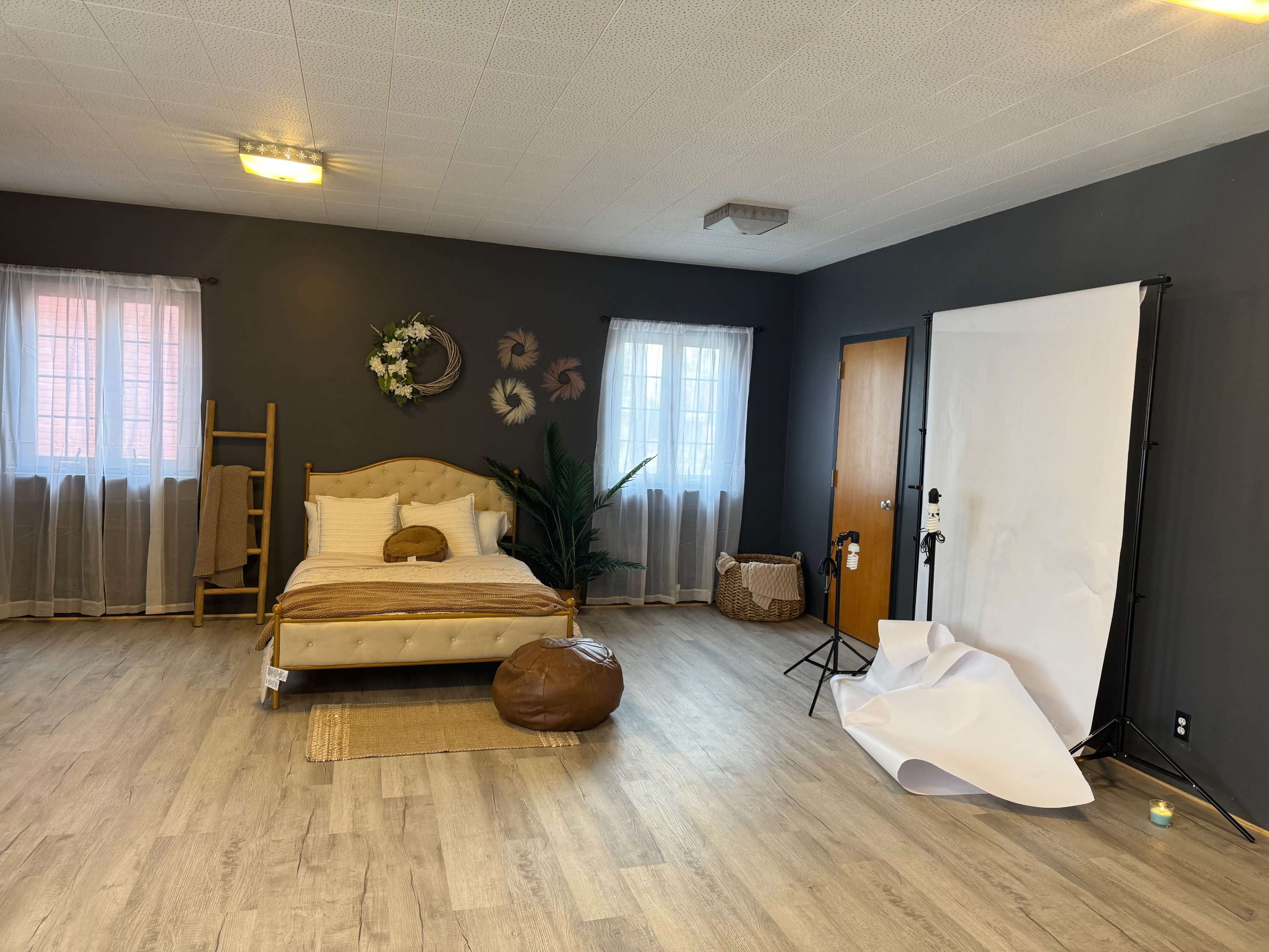 The image shows a spacious room featuring a bed, a ladder, a large white backdrop, and natural light coming through the windows.