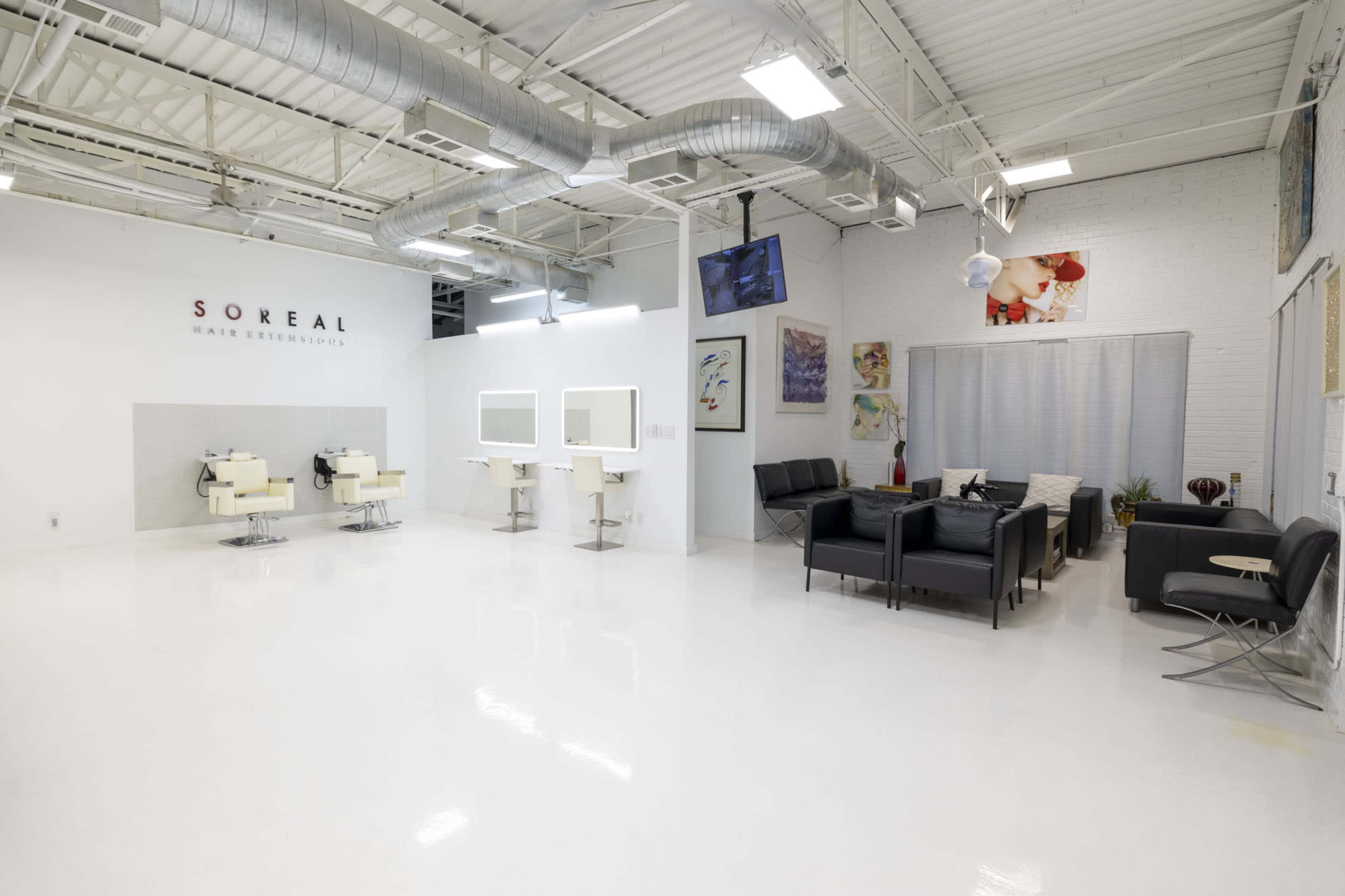 The image shows a modern hair salon with hairdressing stations, a waiting area with black seating, and white walls.