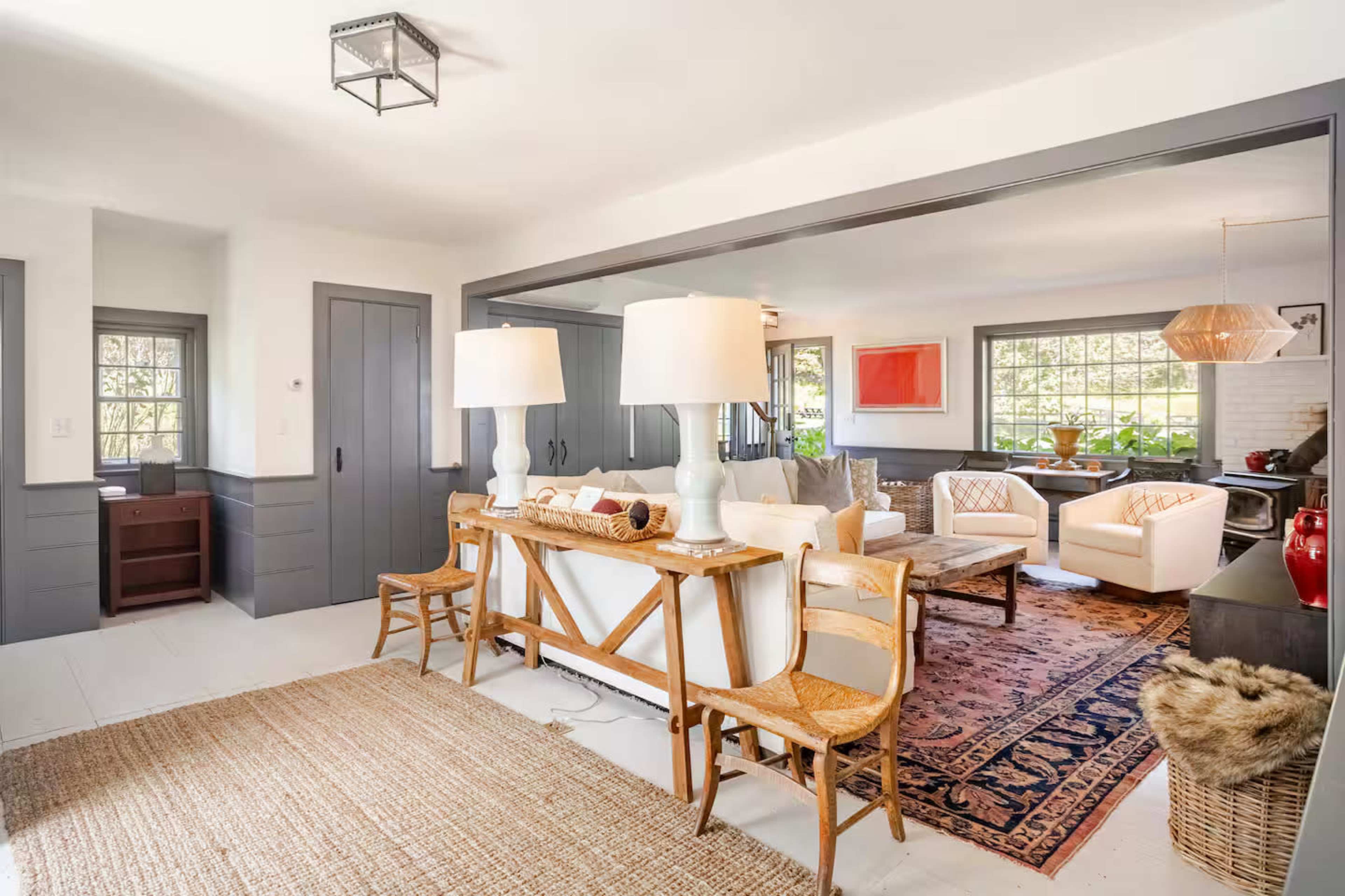 The image shows a living space with a dining area, featuring a wooden table with two large lamps, chairs, and a cozy arrangement of white sofas and a coffee table in the background.