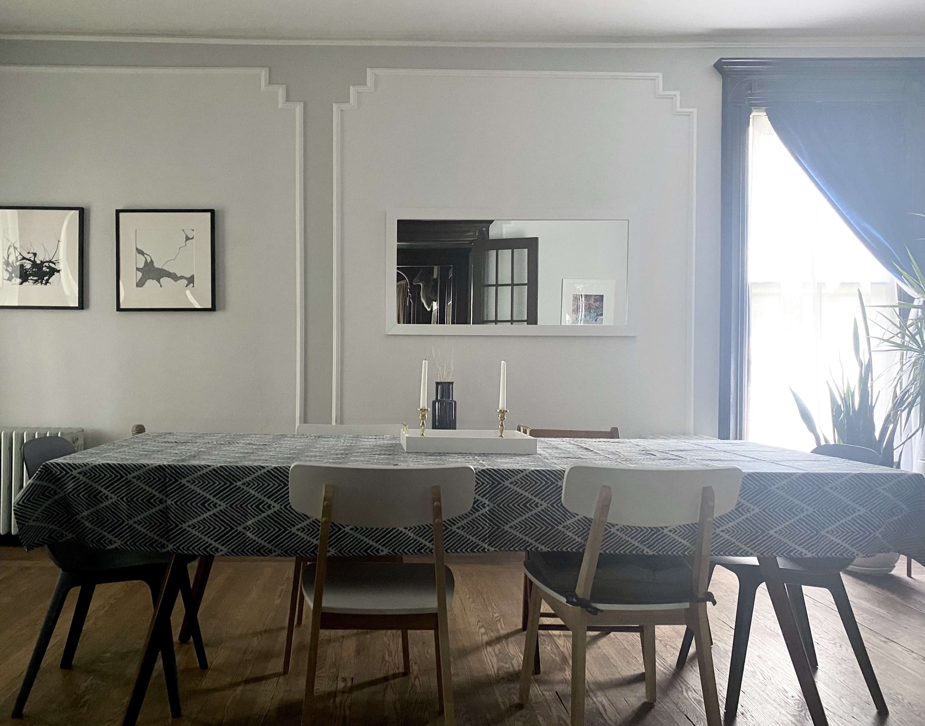 A spacious dining room features a long table set with a patterned tablecloth, two candles, and framed artwork on the walls.
