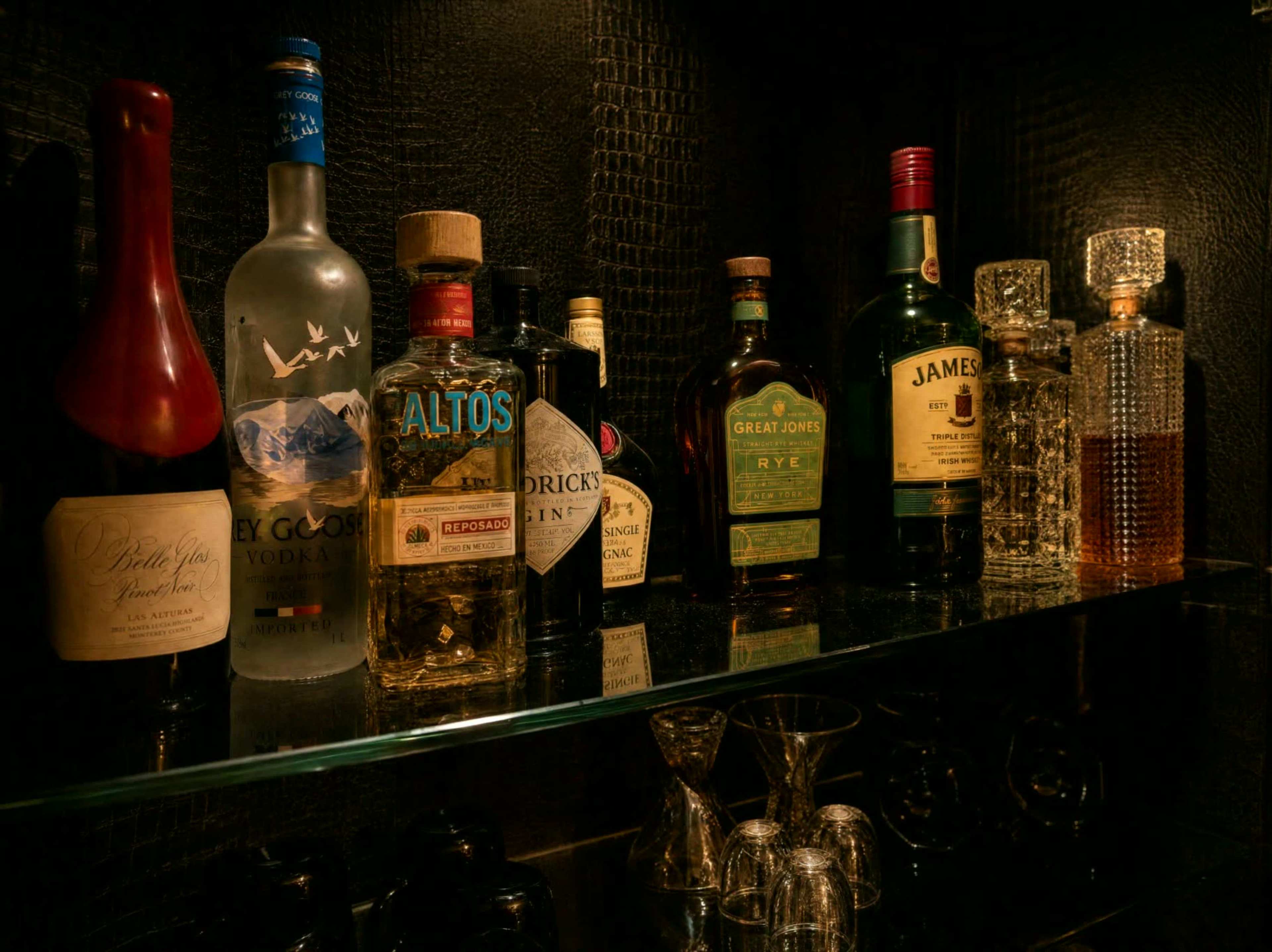 A variety of liquor bottles, including vodka, tequila, whiskey, and rum, are arranged neatly on a glass shelf against a dark textured background.