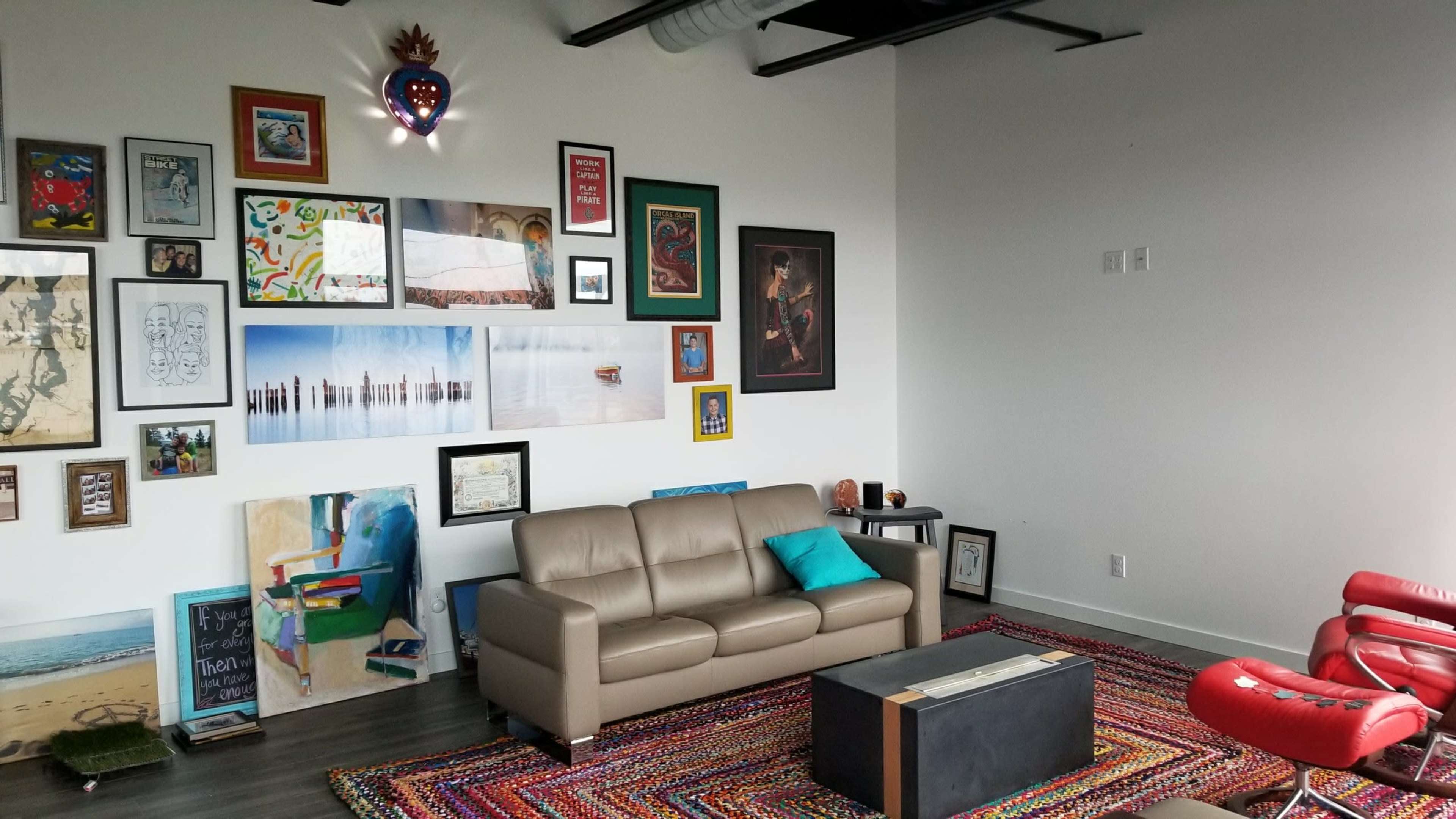 A modern living room with a light-colored sofa, a colorful rug, and a wall adorned with a diverse collection of framed artwork.