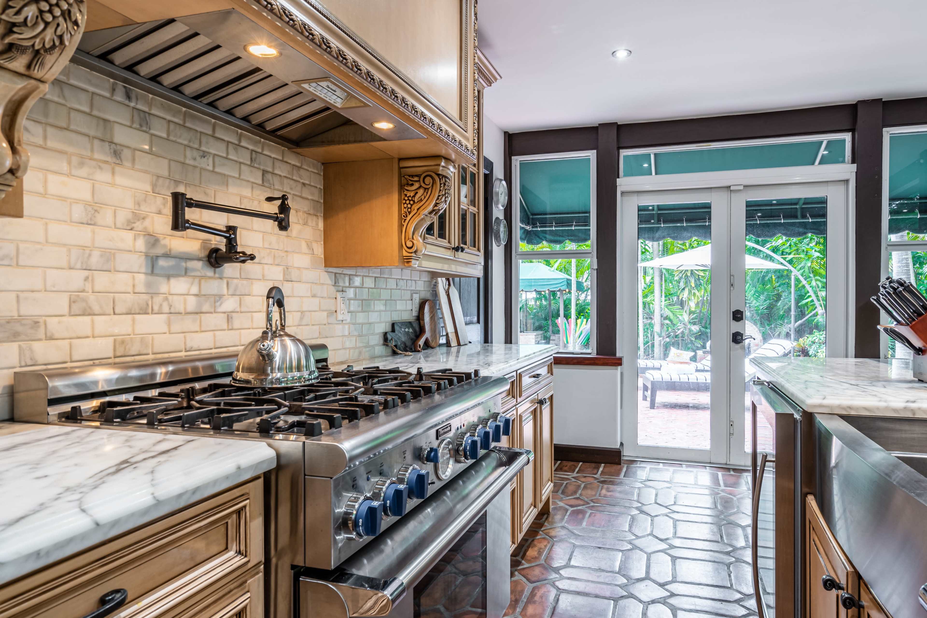 A kitchen with a marble countertop, a gas stove with multiple burners, and double doors leading to an outdoor seating area.