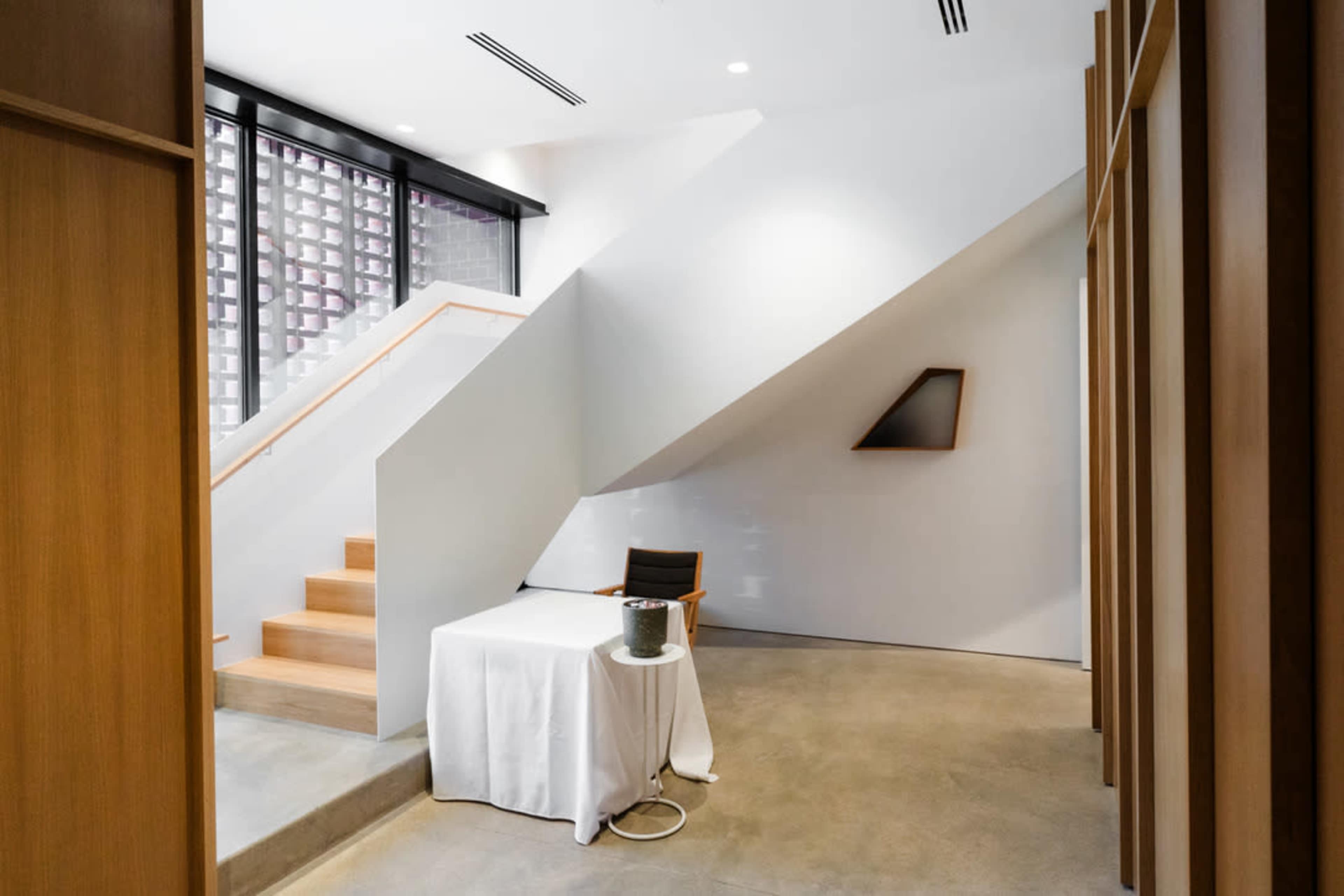The interior space features a minimalist design with a staircase, a table draped in white cloth, and warm wooden accents.