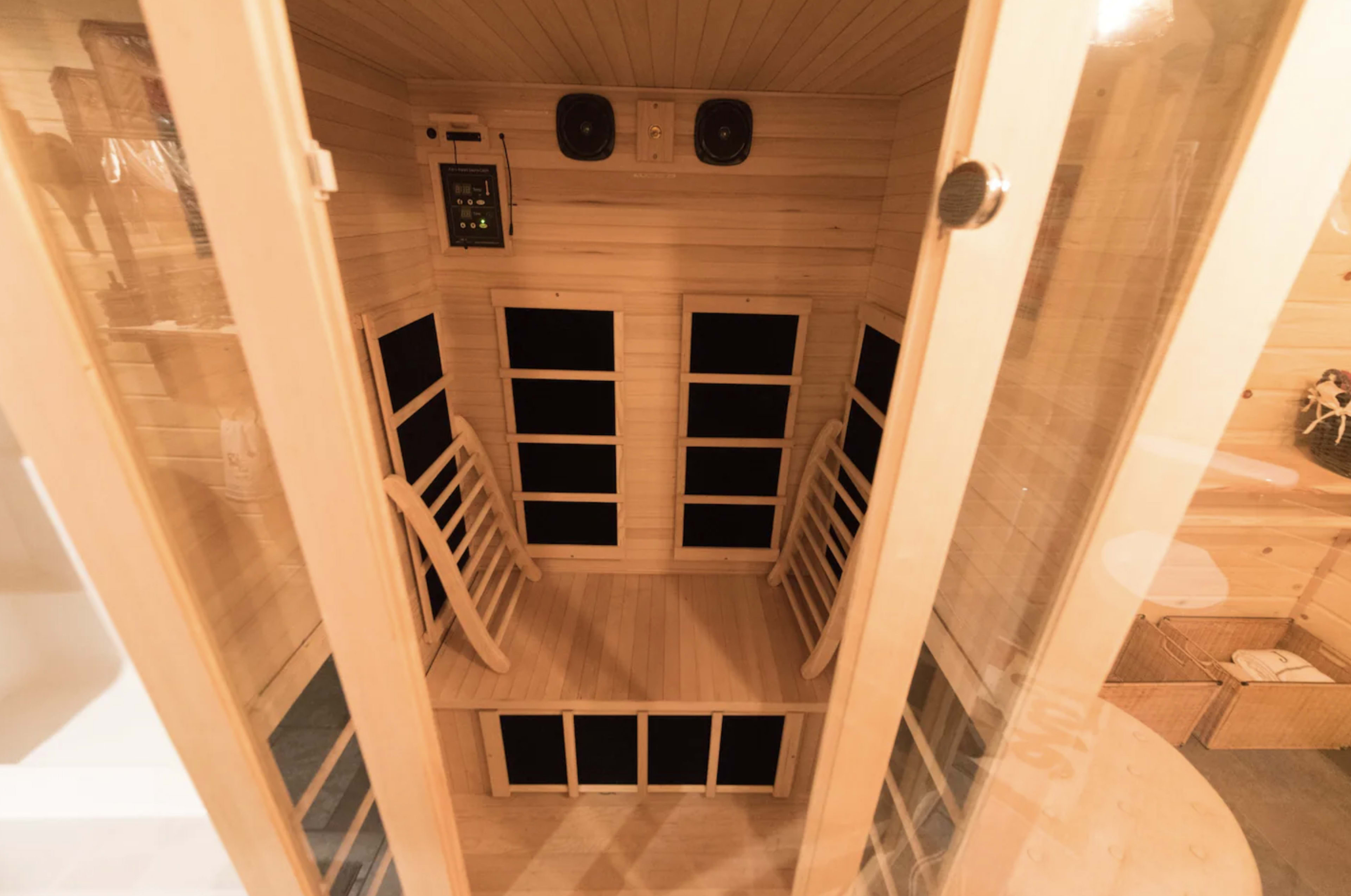 The image shows the interior of a wooden sauna equipped with benches, speakers, and a control panel.