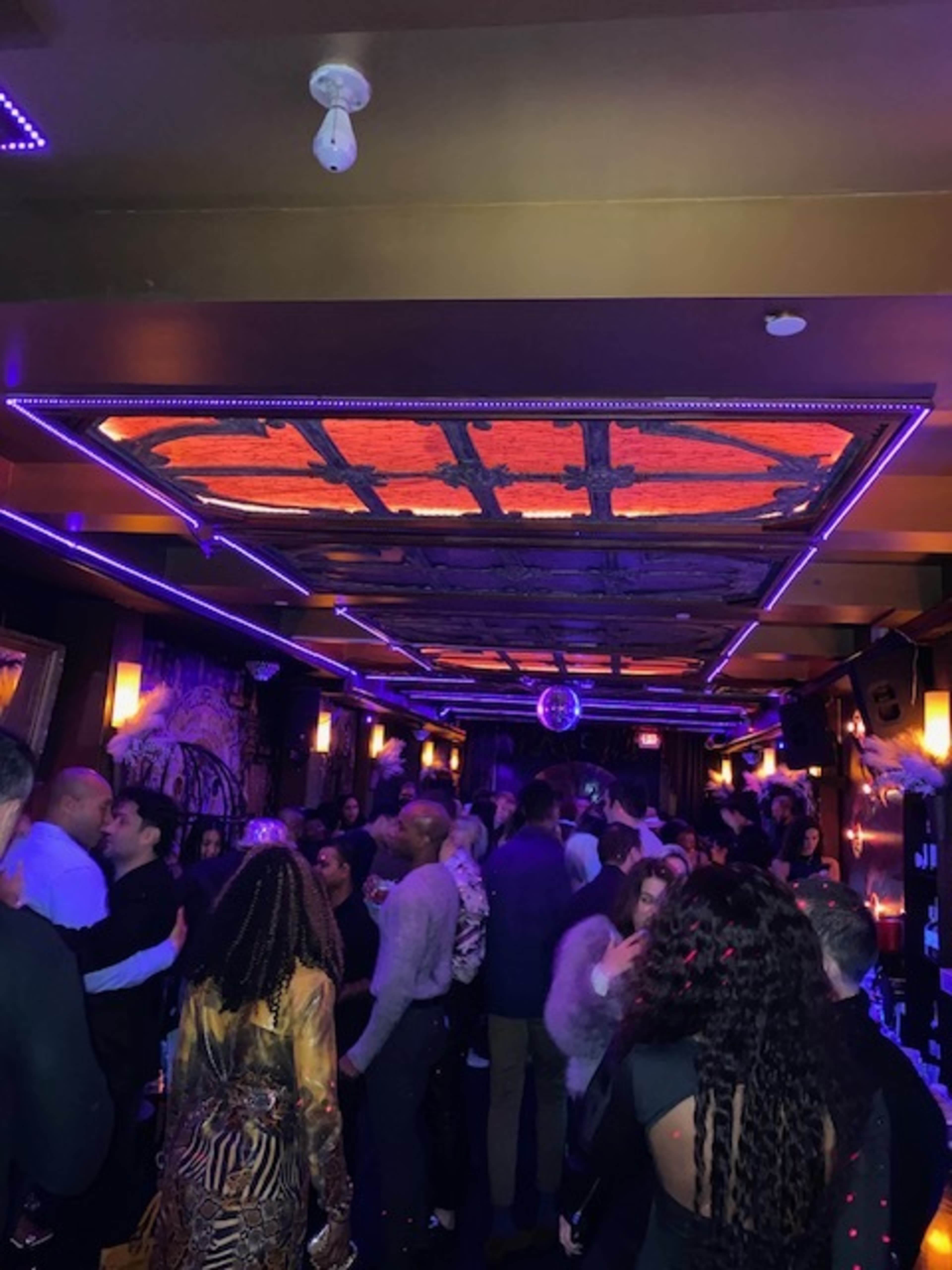 A crowded nightclub scene features a mix of people socializing under colorful lighting and a disco ball.