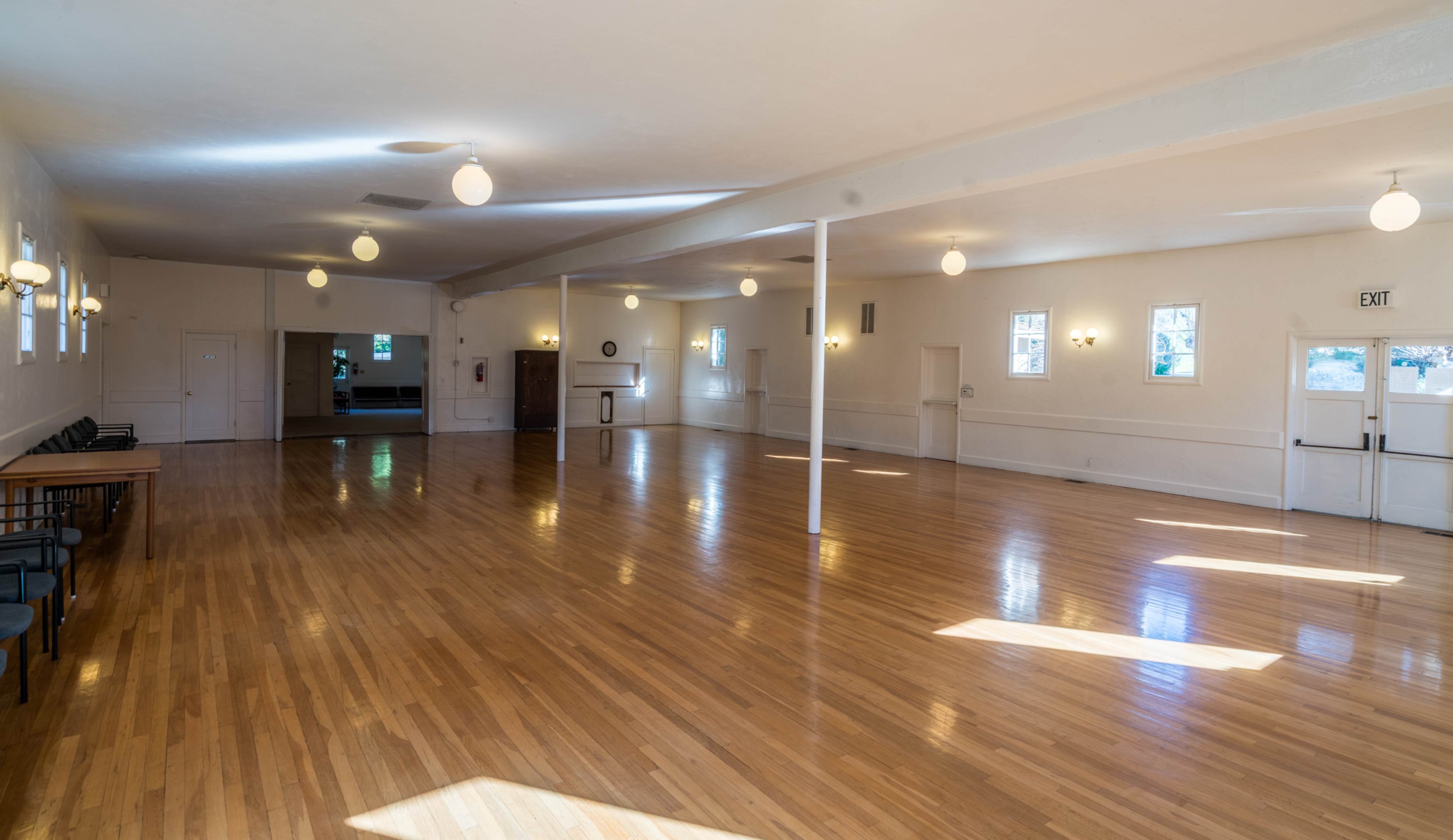 A spacious, well-lit room with polished wooden floors, white walls, and several round overhead lights.