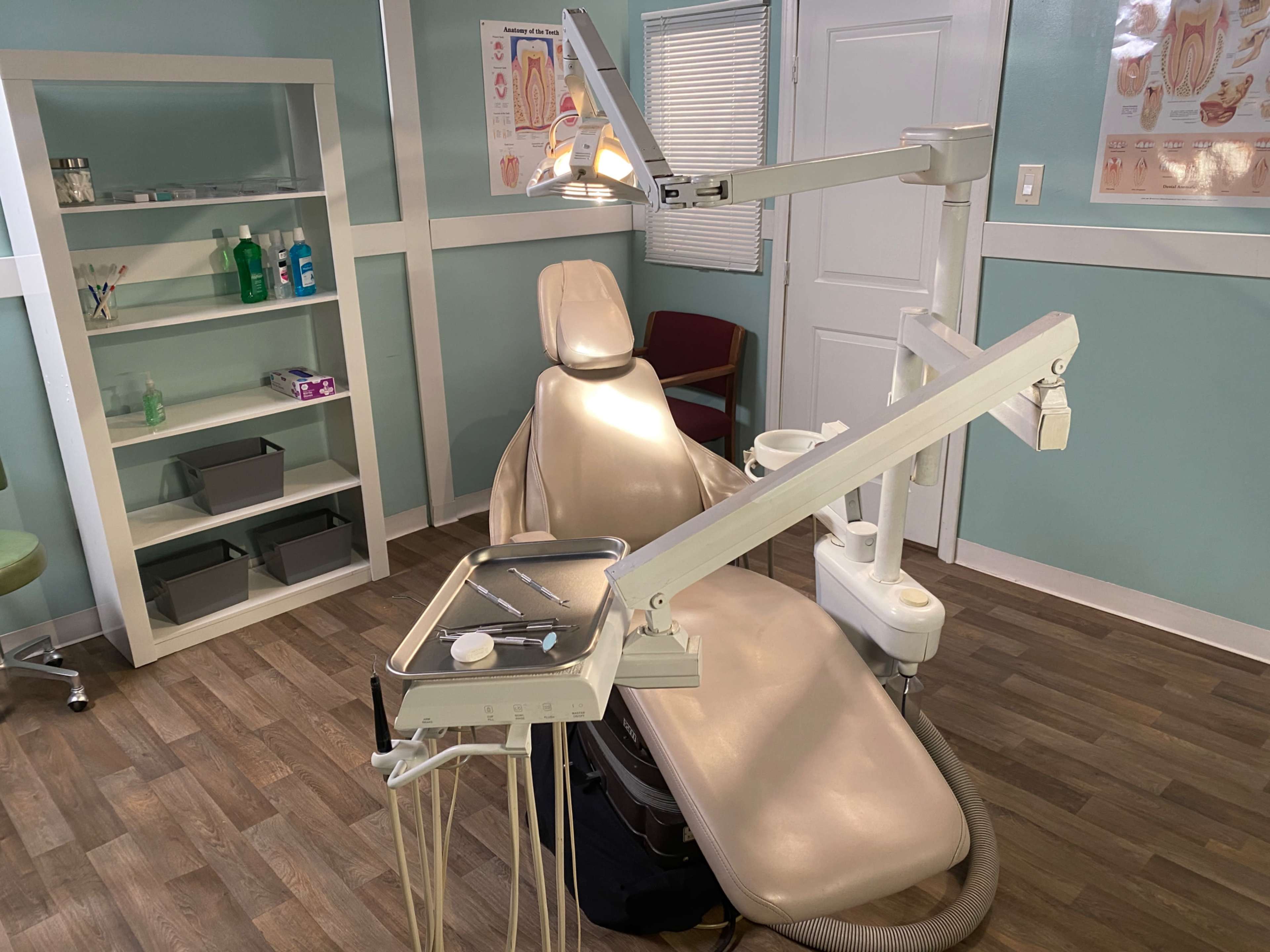 The image shows a dental examination room featuring a dentist's chair, overhead lights, and various dental tools arranged on a tray.