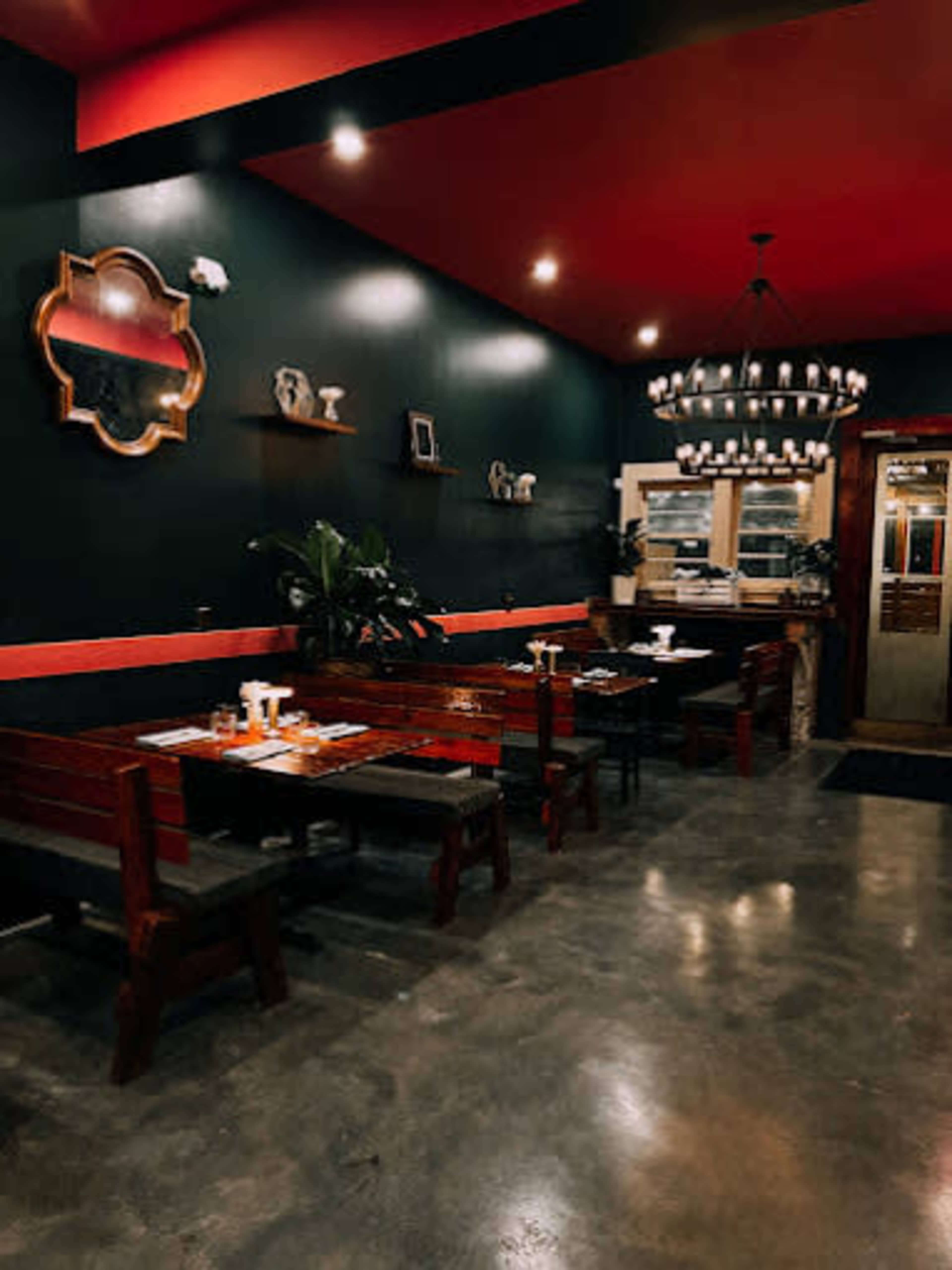 The interior of a restaurant features wooden benches, a chandelier, and dark green walls with red accents.