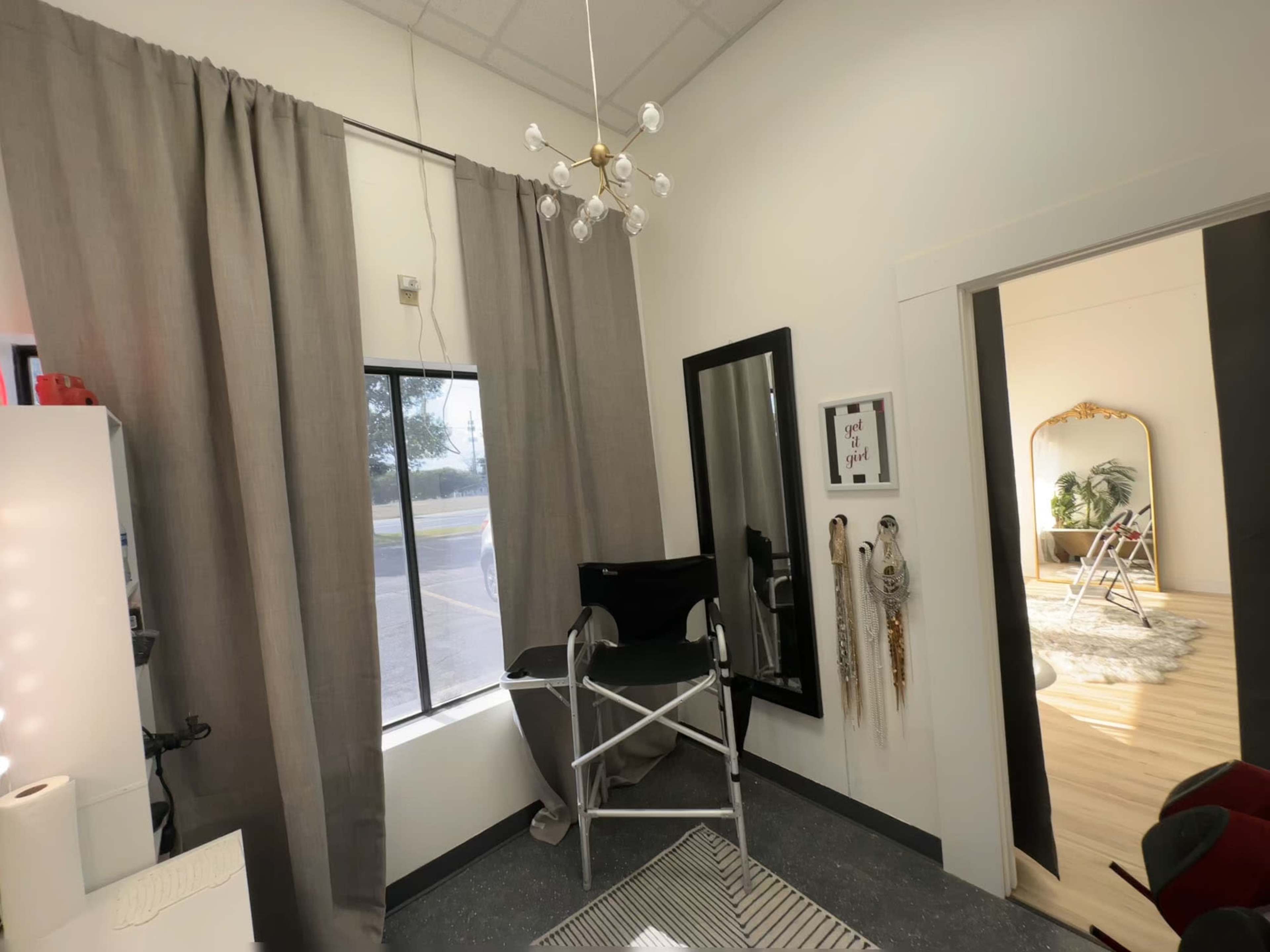 A well-lit room featuring a tall chair beside a window draped with gray curtains, a mirror on the wall, and a decorative rug on the floor.