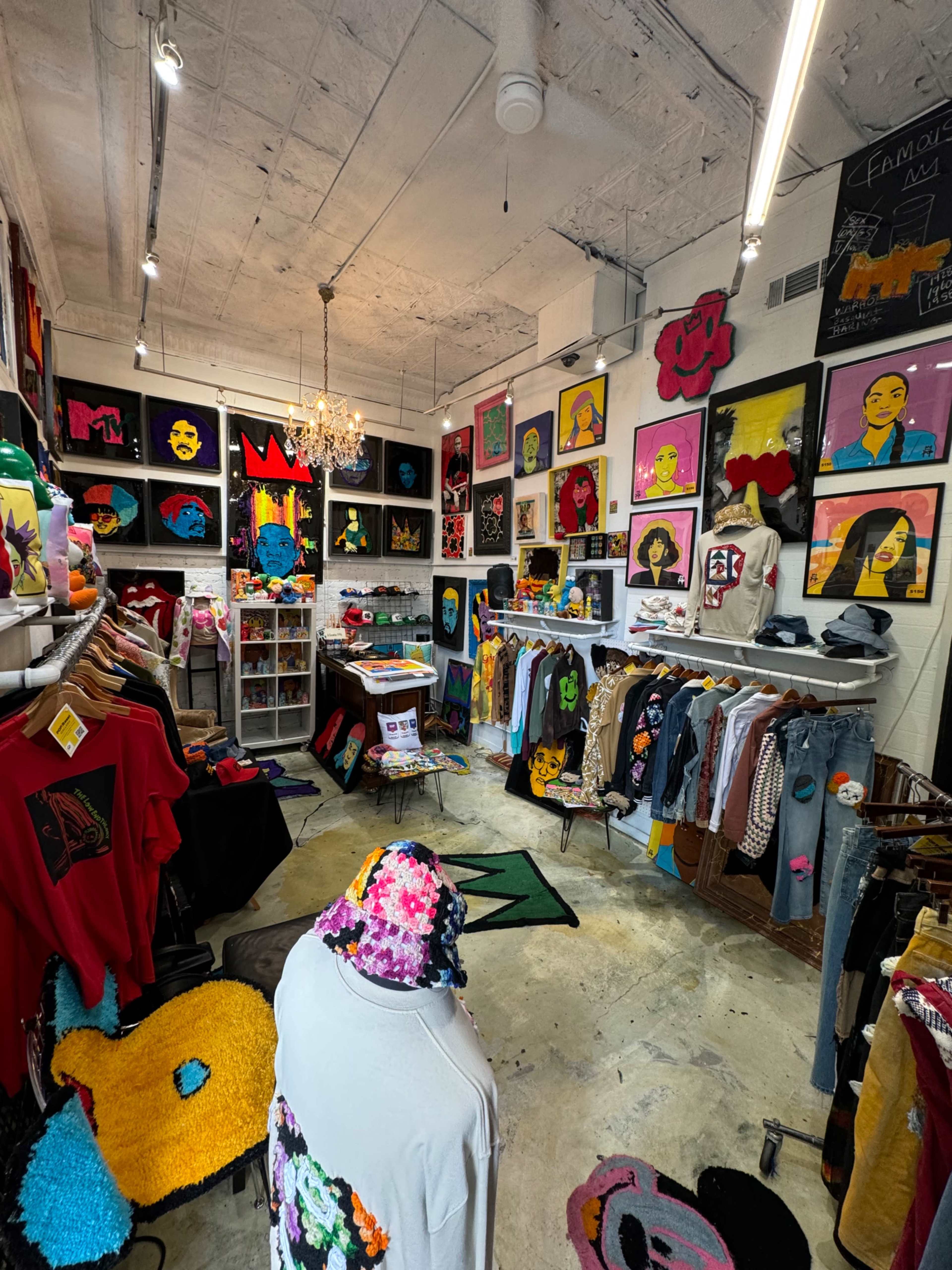 The image shows an eclectic retail space featuring colorful clothing displays and vibrant artwork on the walls.