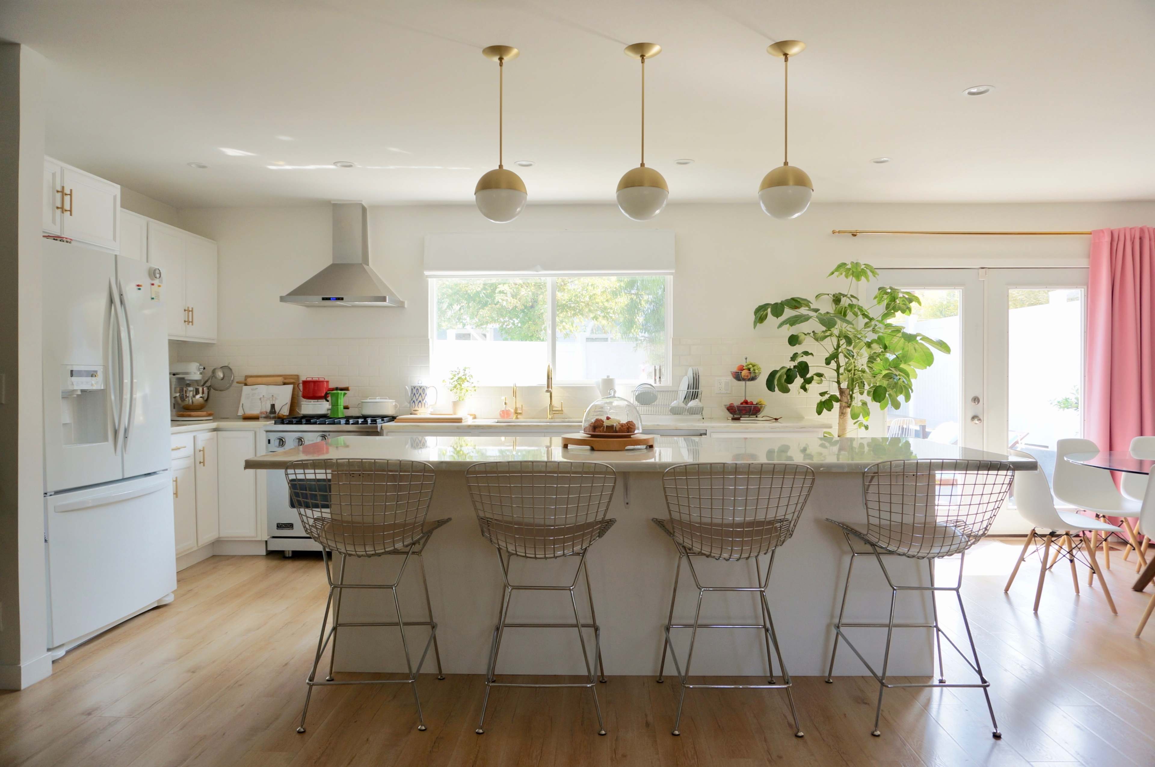 A modern kitchen with a large island, metallic bar stools, and ample natural light from a window and sliding doors.