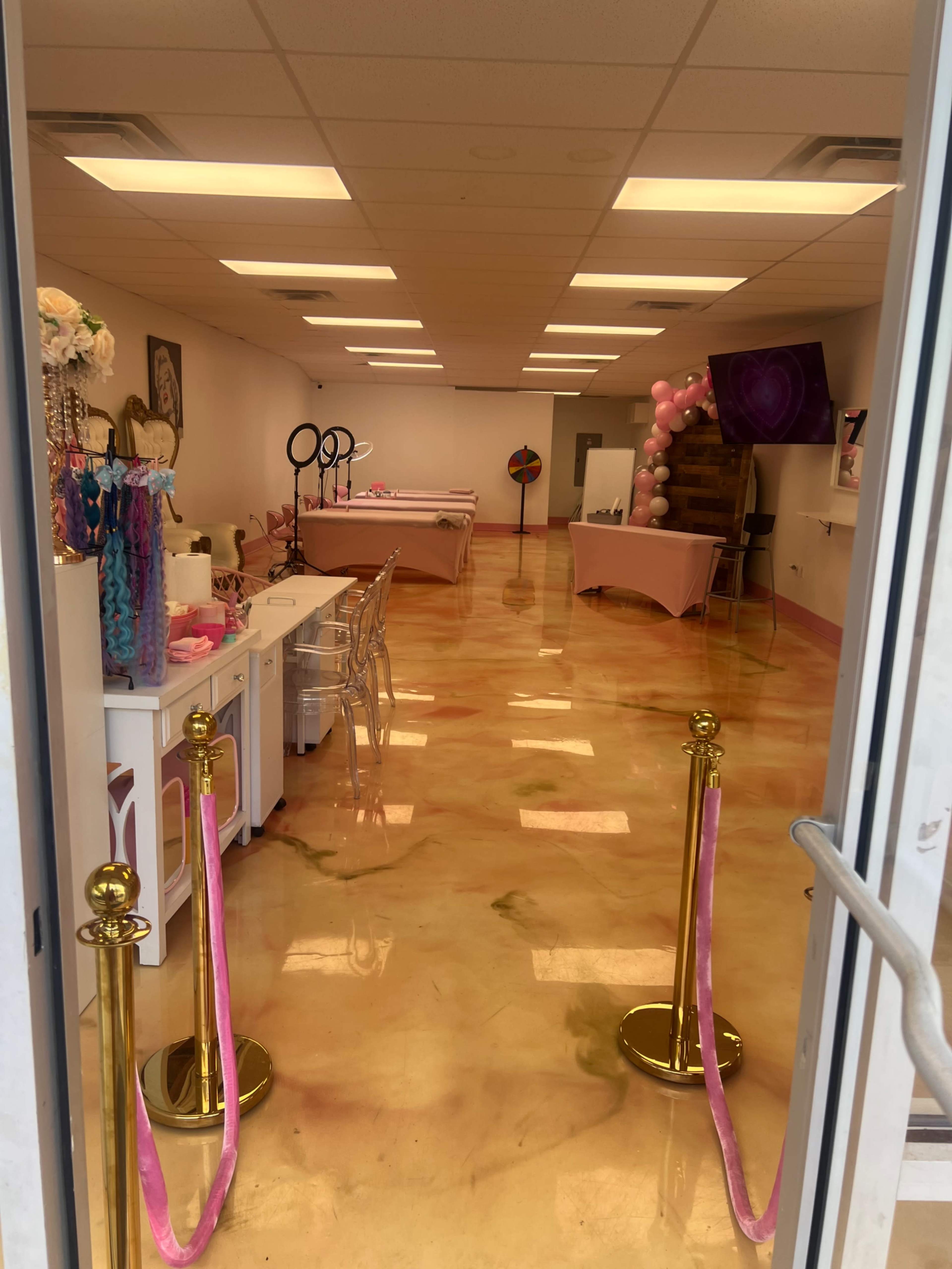 The image shows the interior of a brightly lit, pink-themed studio with glossy orange and yellow floors and decorated tables set up for an event.