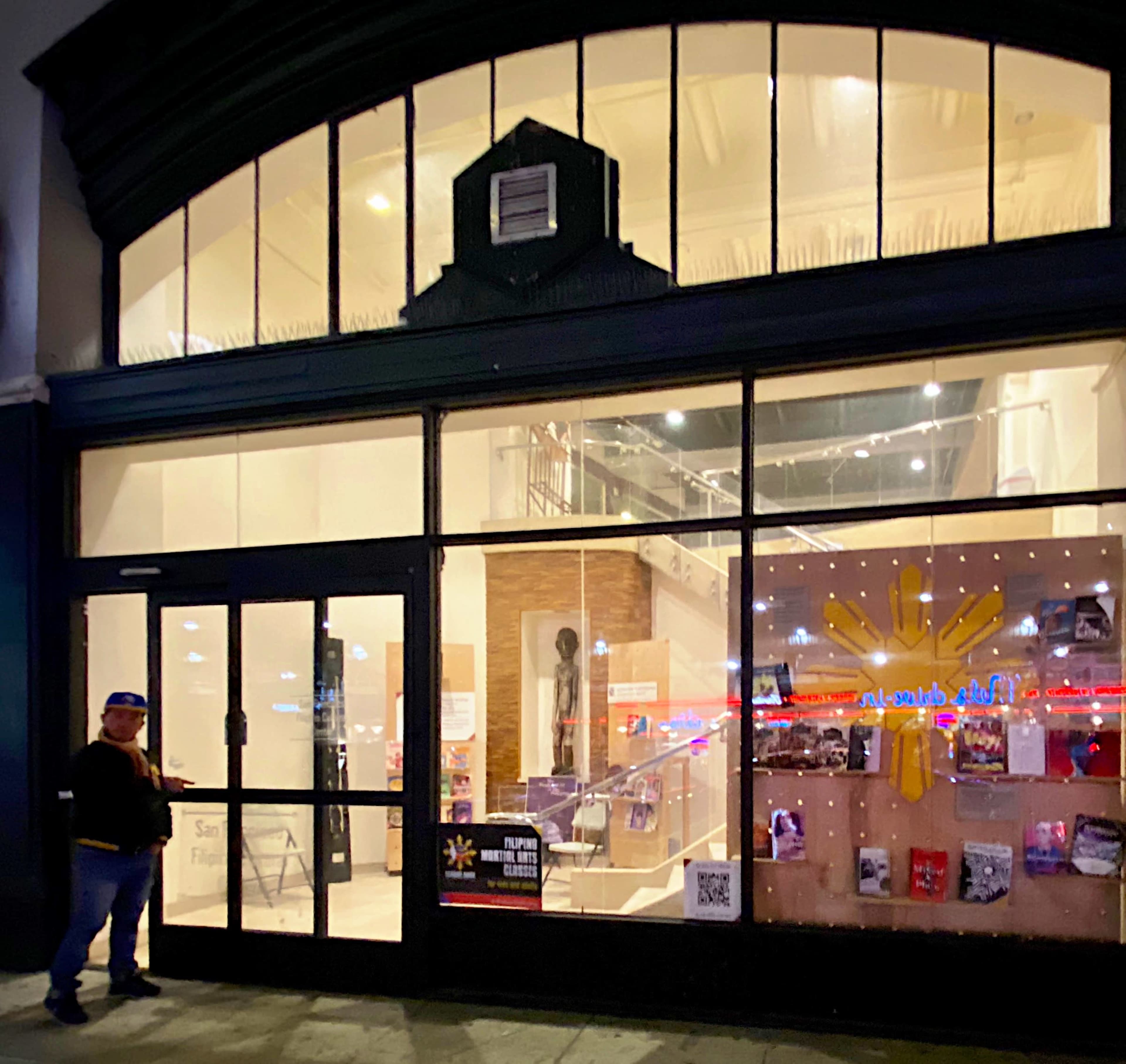 A person stands by a glass entrance of a building with visible signage and displayed items inside.