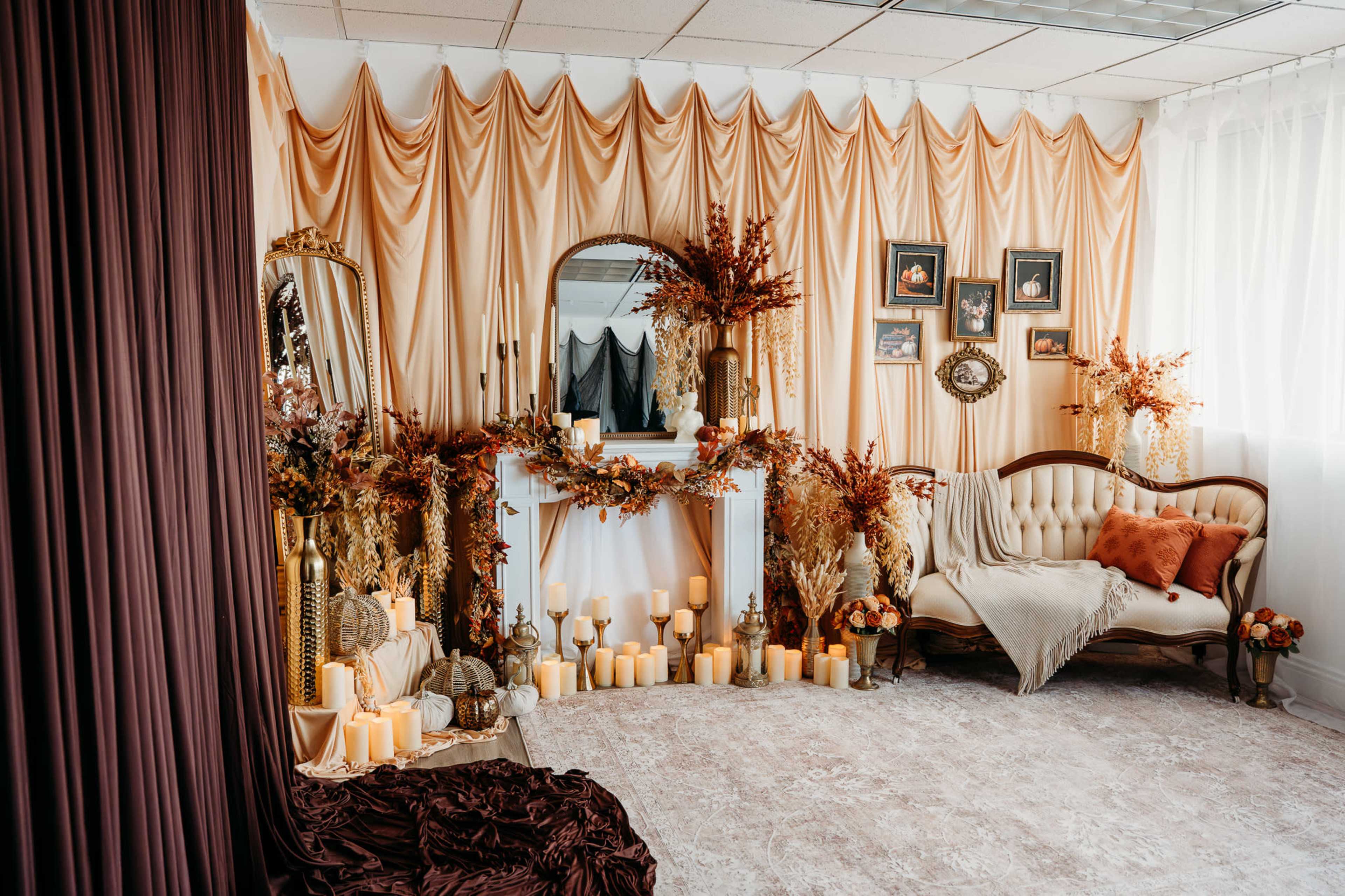 The image shows a decorated room with draped fabric in soft hues, a vintage sofa, a mirror, and various candles arranged among floral decorations.