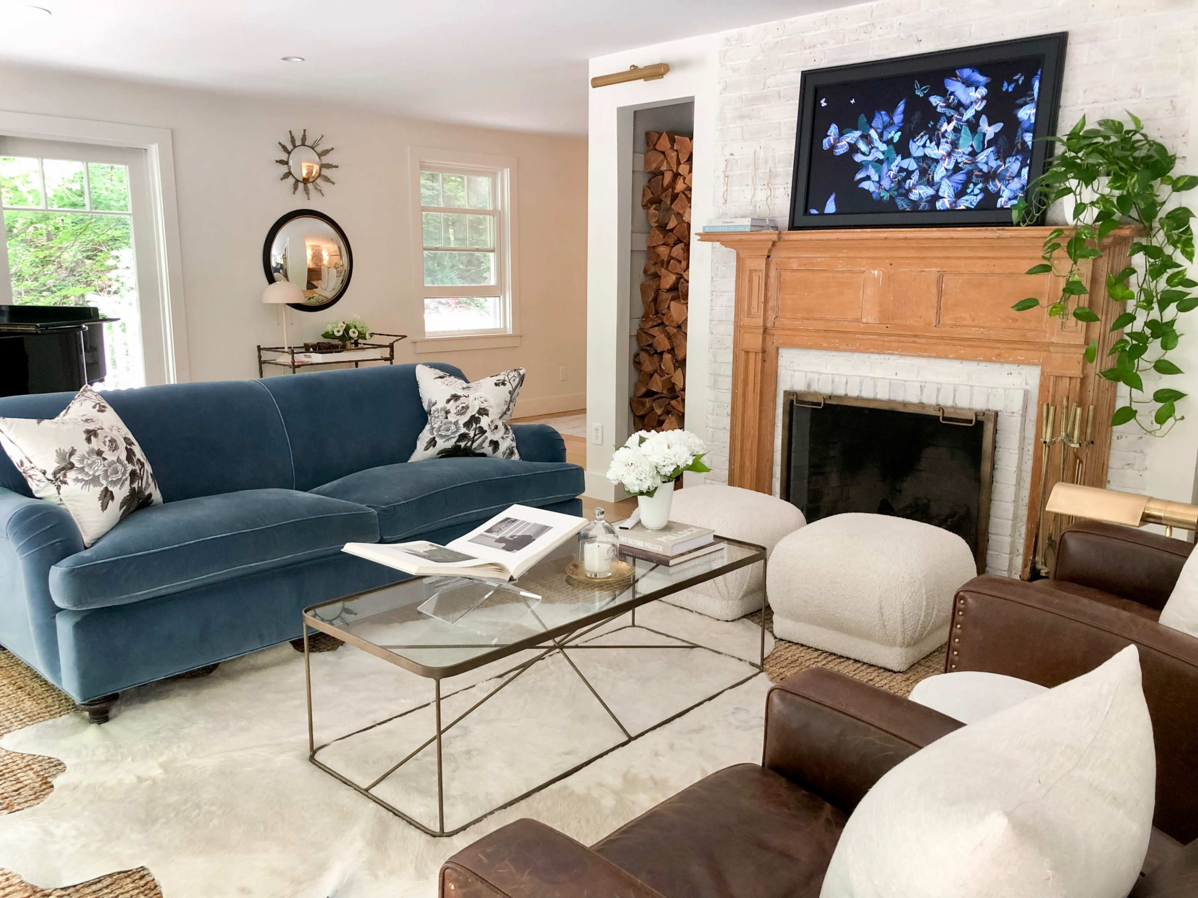 The living room features a blue velvet sofa, brown leather armchairs, a glass coffee table, and a fireplace with wooden logs stacked nearby.
