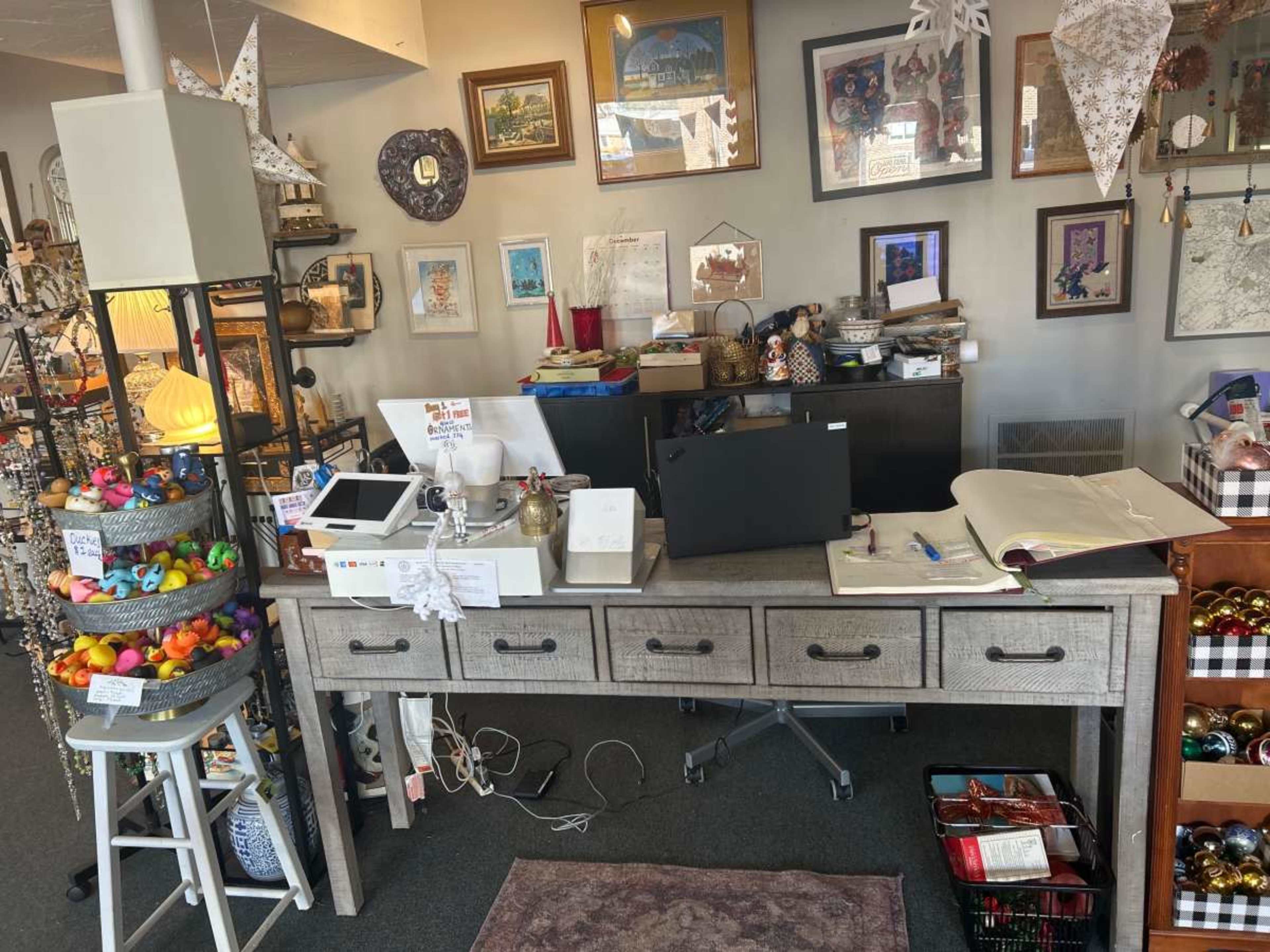 A cluttered workspace displays various items, including art supplies, decorations, and a computer setup, with decorative objects arranged on shelves in the background.
