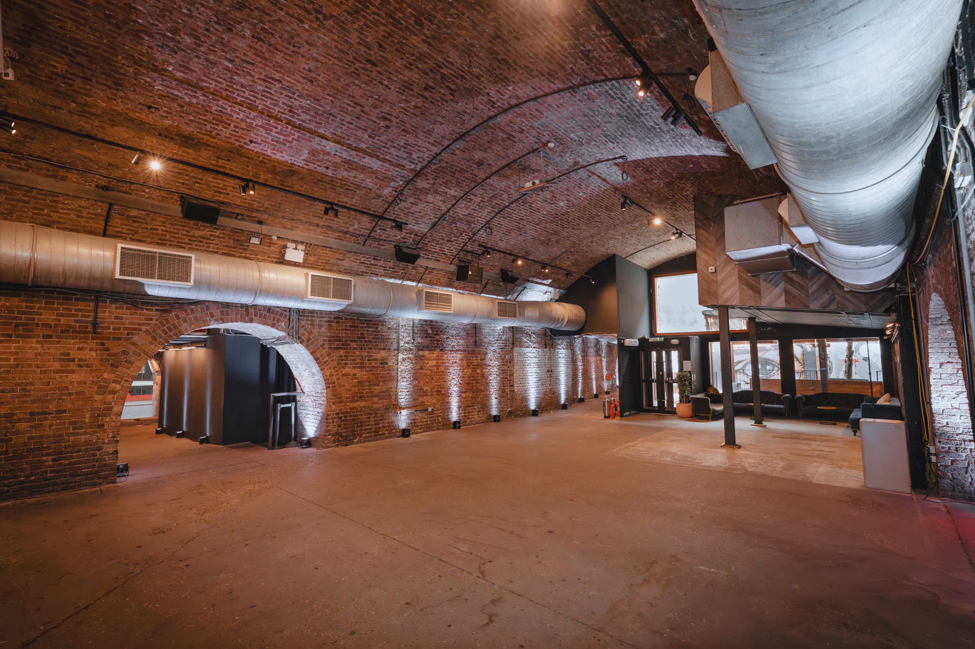 The image shows an industrial space with arched brick walls, exposed ductwork, and a large open area featuring a polished concrete floor.