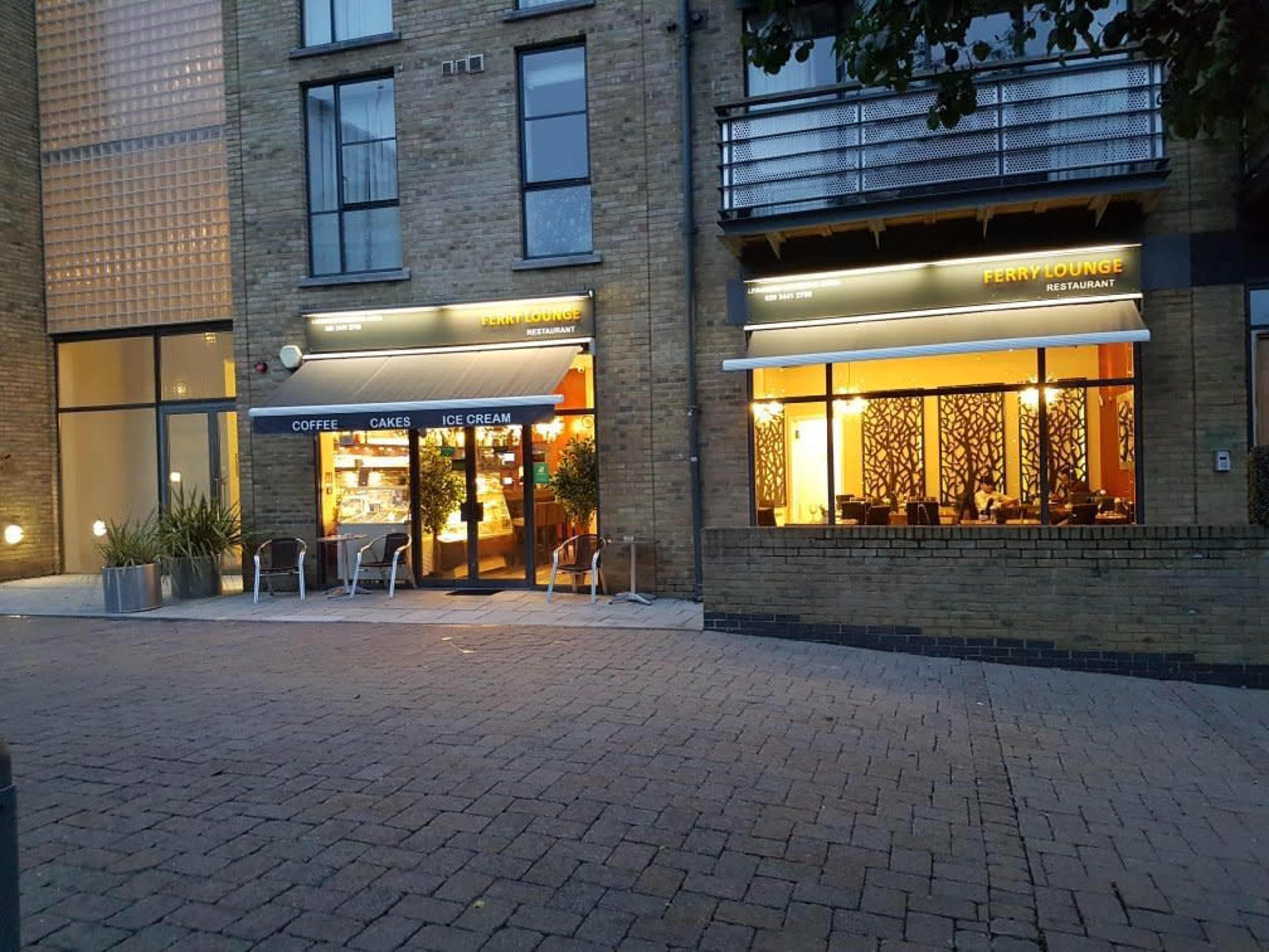 A building with two restaurant entrances, Ferry Lounge and another café, set in a brick exterior with outdoor seating.
