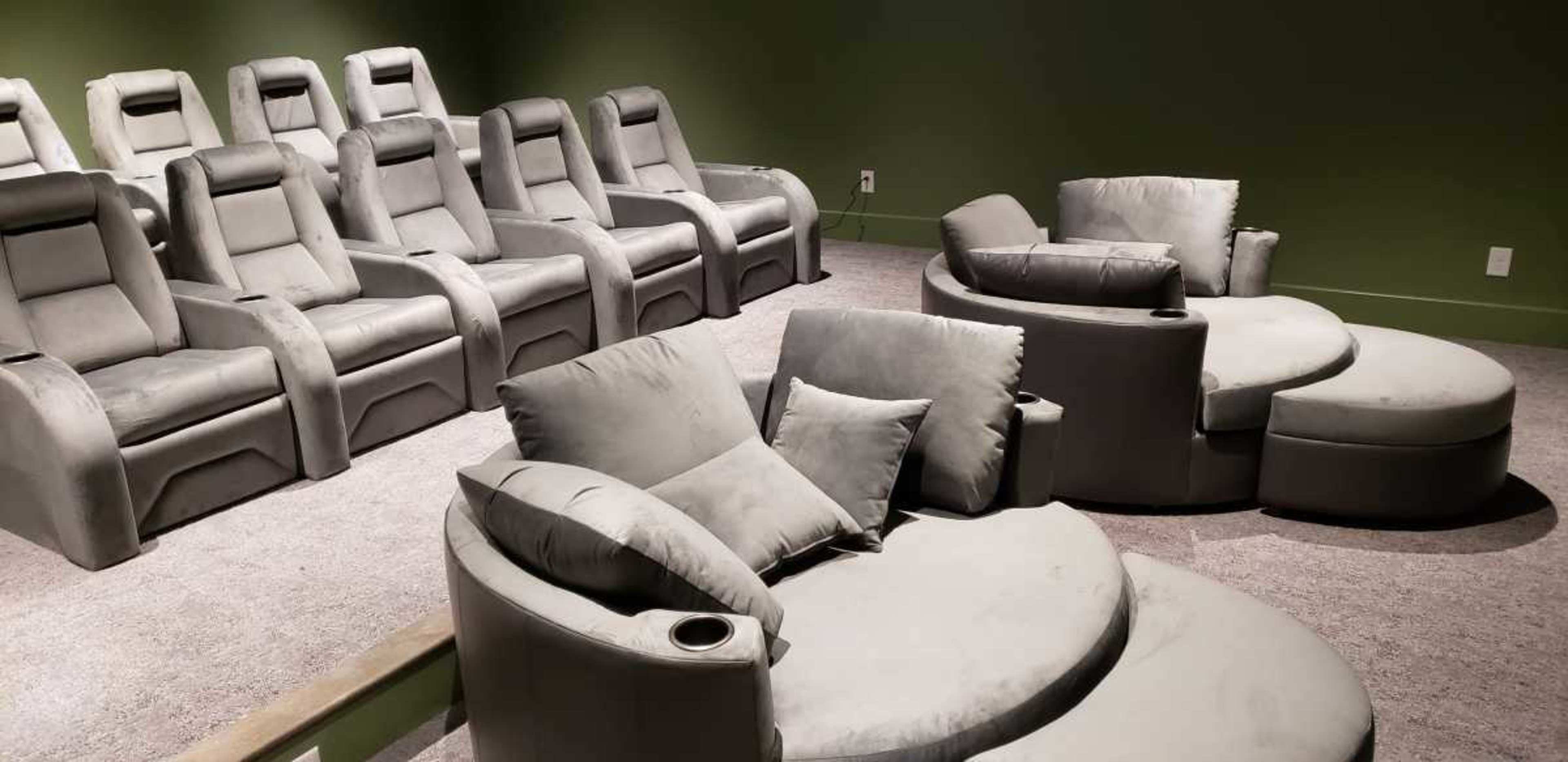 A home theater setup with seven upholstered recliner seats in a row and a circular lounge seating area with cushions.