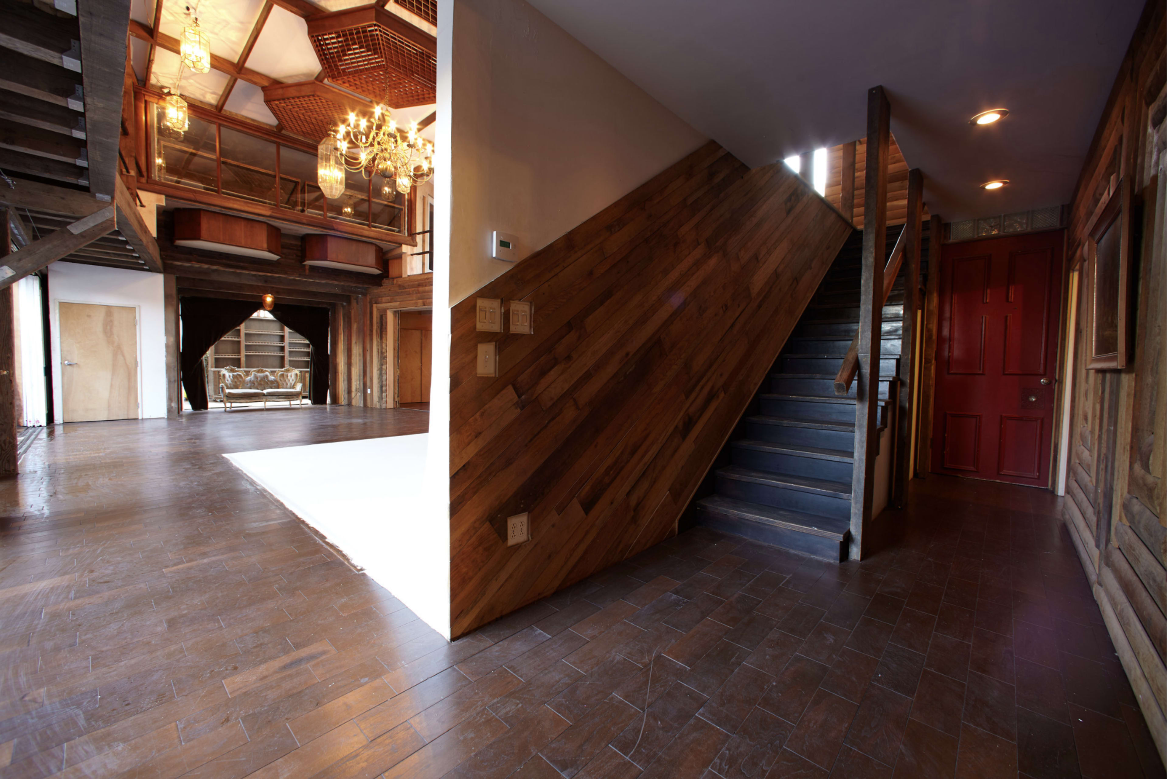 The image shows a spacious entryway with a wooden staircase leading to an upper level, featuring large windows and a rustic chandelier overhead.