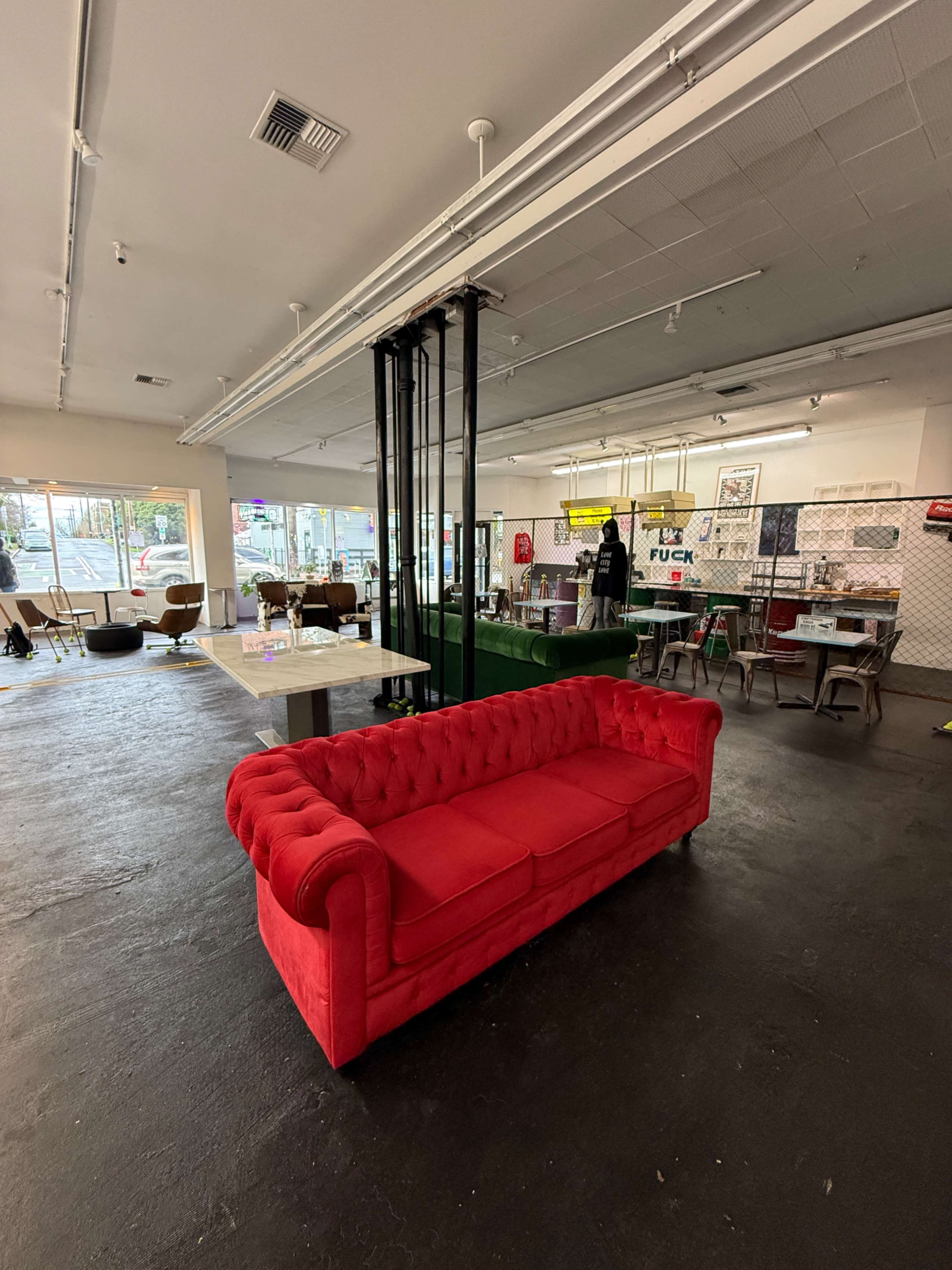 A red tufted couch is positioned in the center of a spacious interior filled with various tables and chairs.