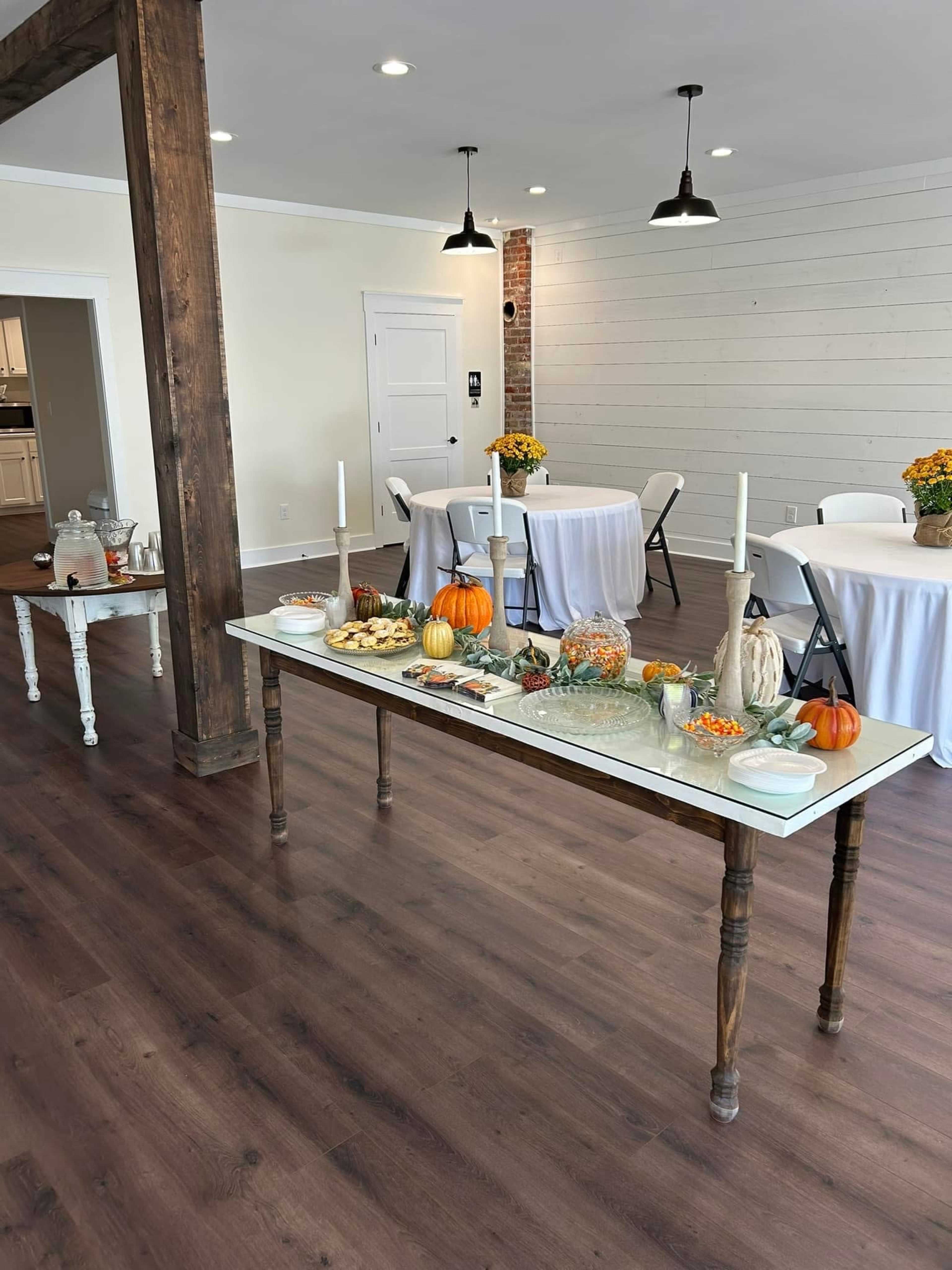 A buffet table is decorated with various dishes and pumpkins, set against a backdrop of a spacious room with white walls and wooden floors.