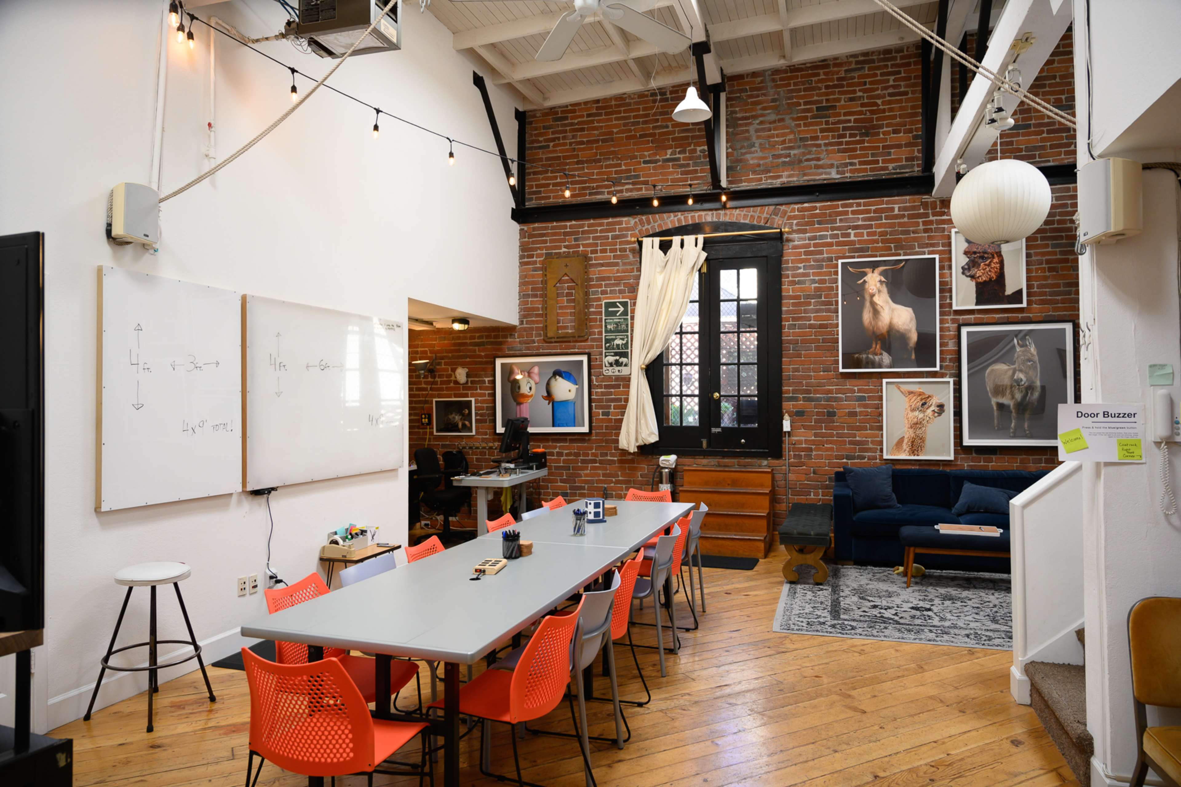 The image shows a spacious, well-lit meeting room with a long table and bright orange chairs, featuring exposed brick walls adorned with animal portraits.