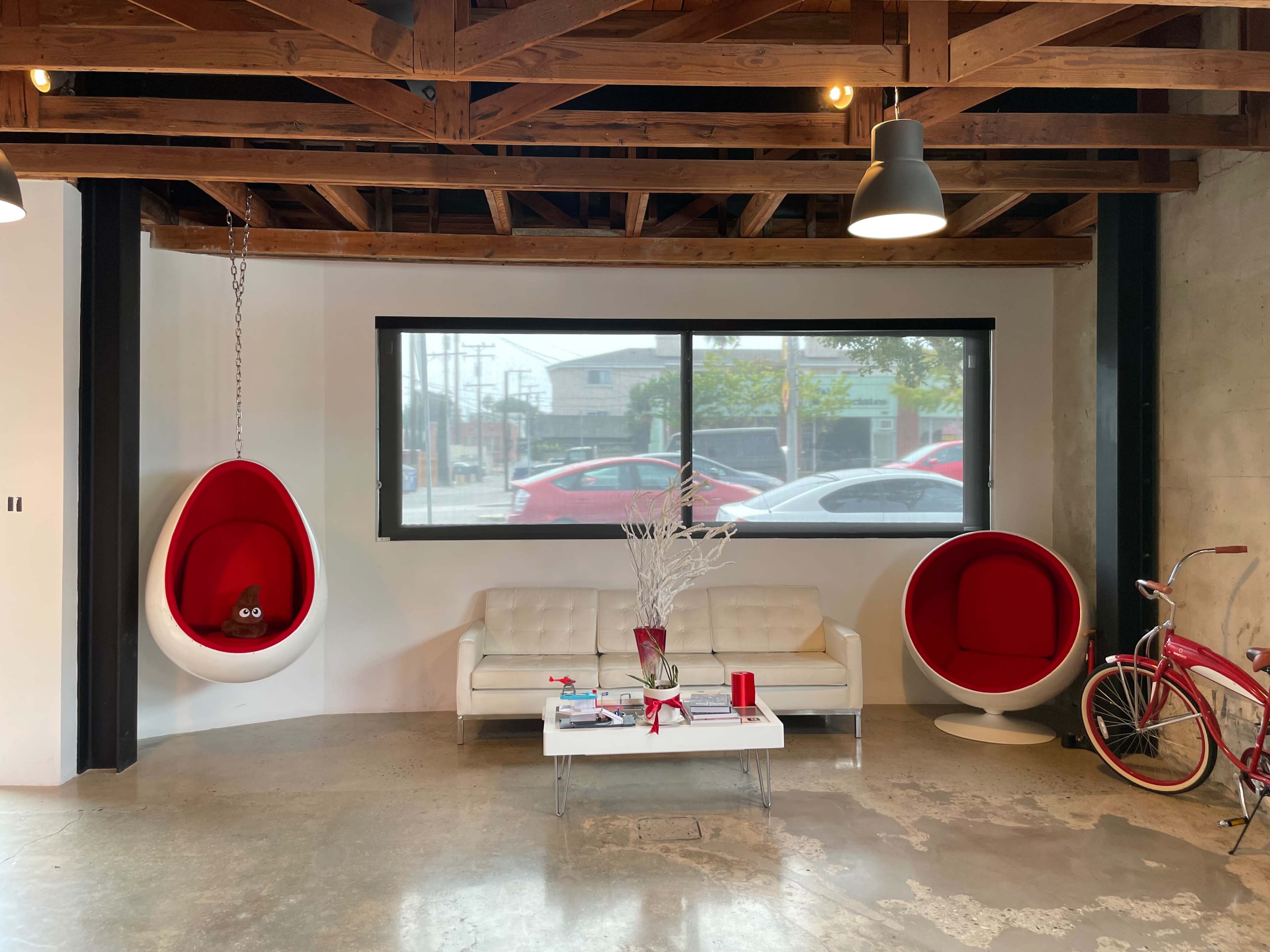 A modern interior space featuring a white sofa, two red hanging chairs, a coffee table, and a decorative bicycle.