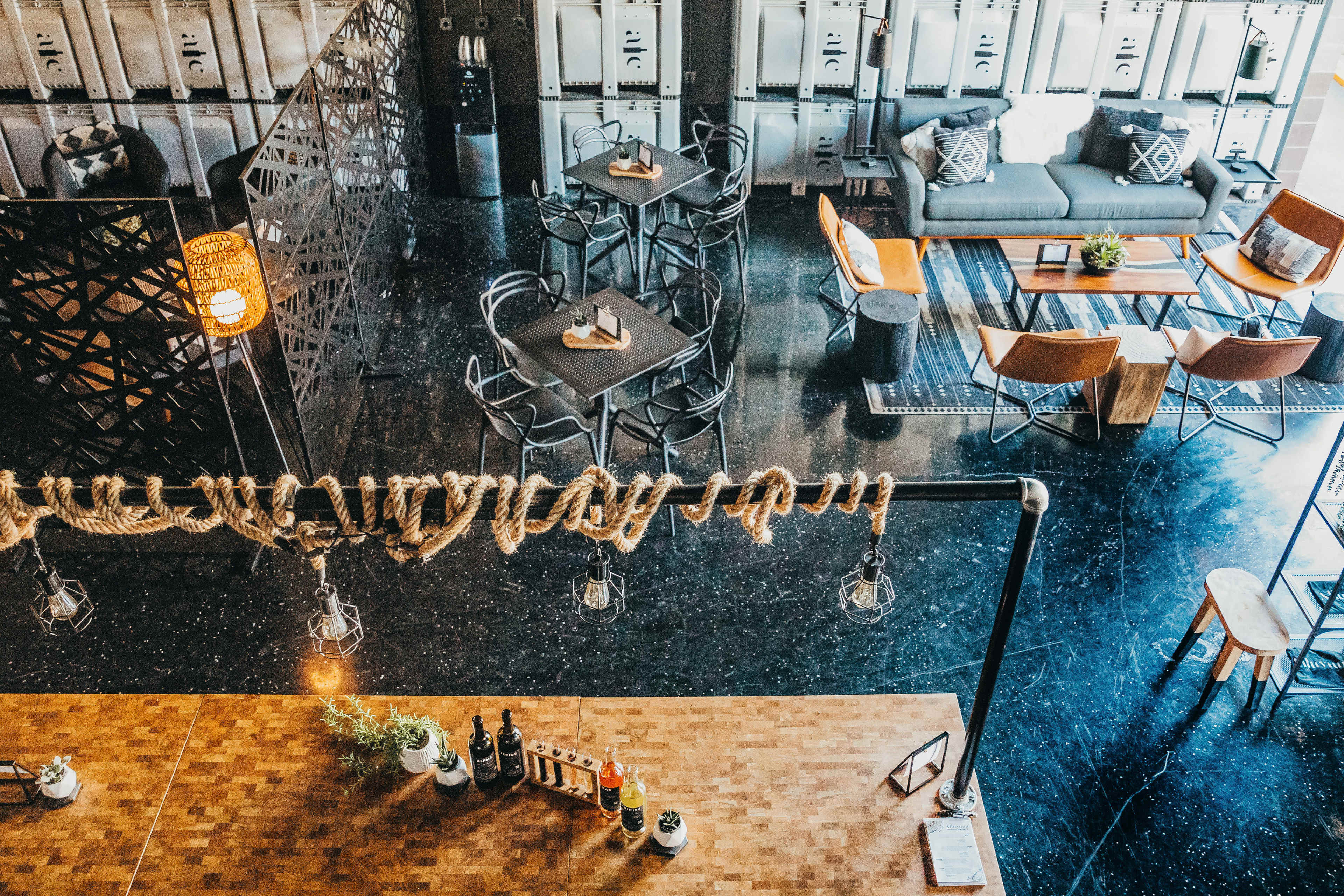 An interior view of a modern café with a wooden bar, seating areas, and a decorative rope light fixture.
