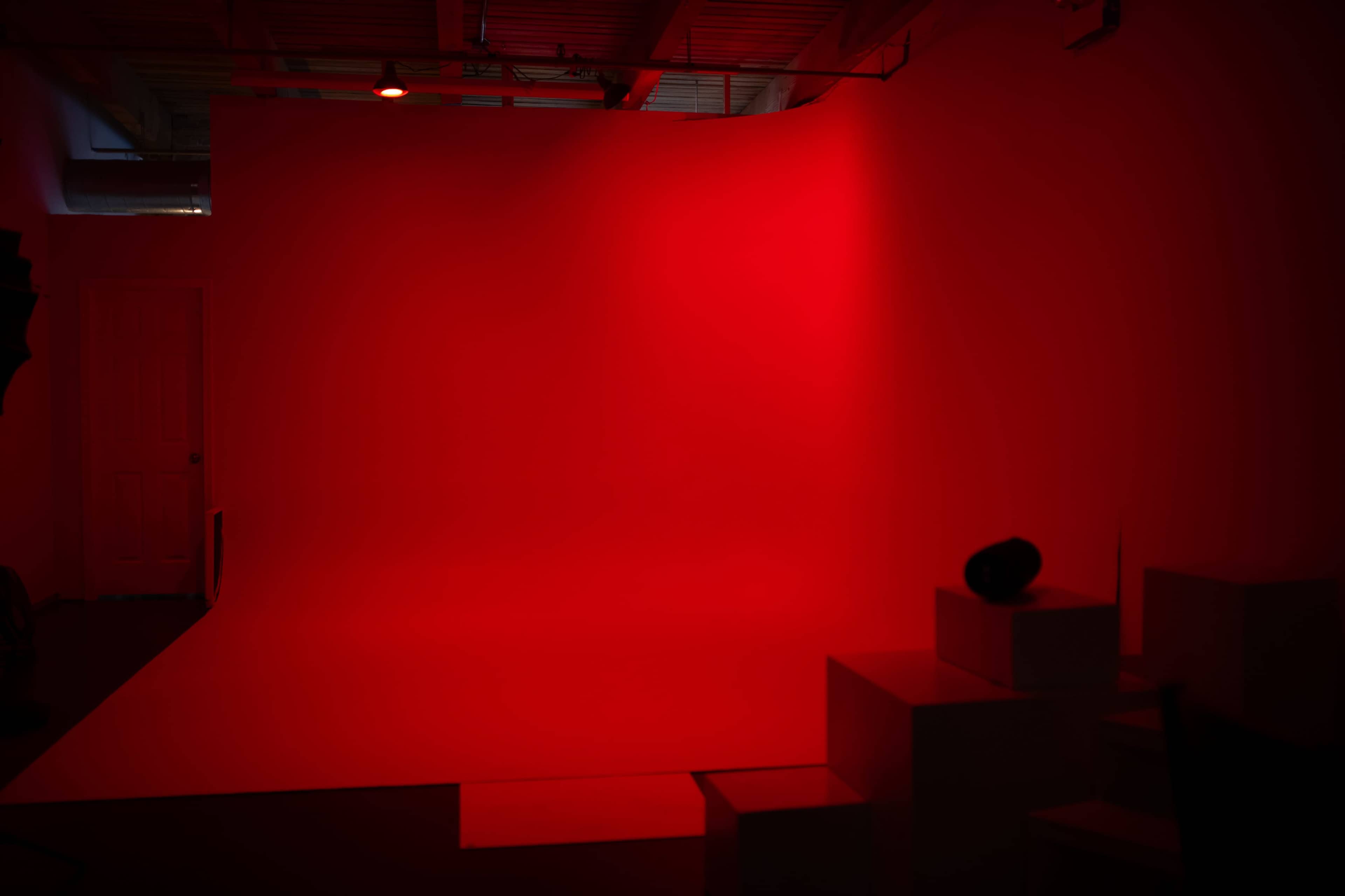 A dimly lit studio space with a bright red backdrop and several white boxes arranged in front of it.