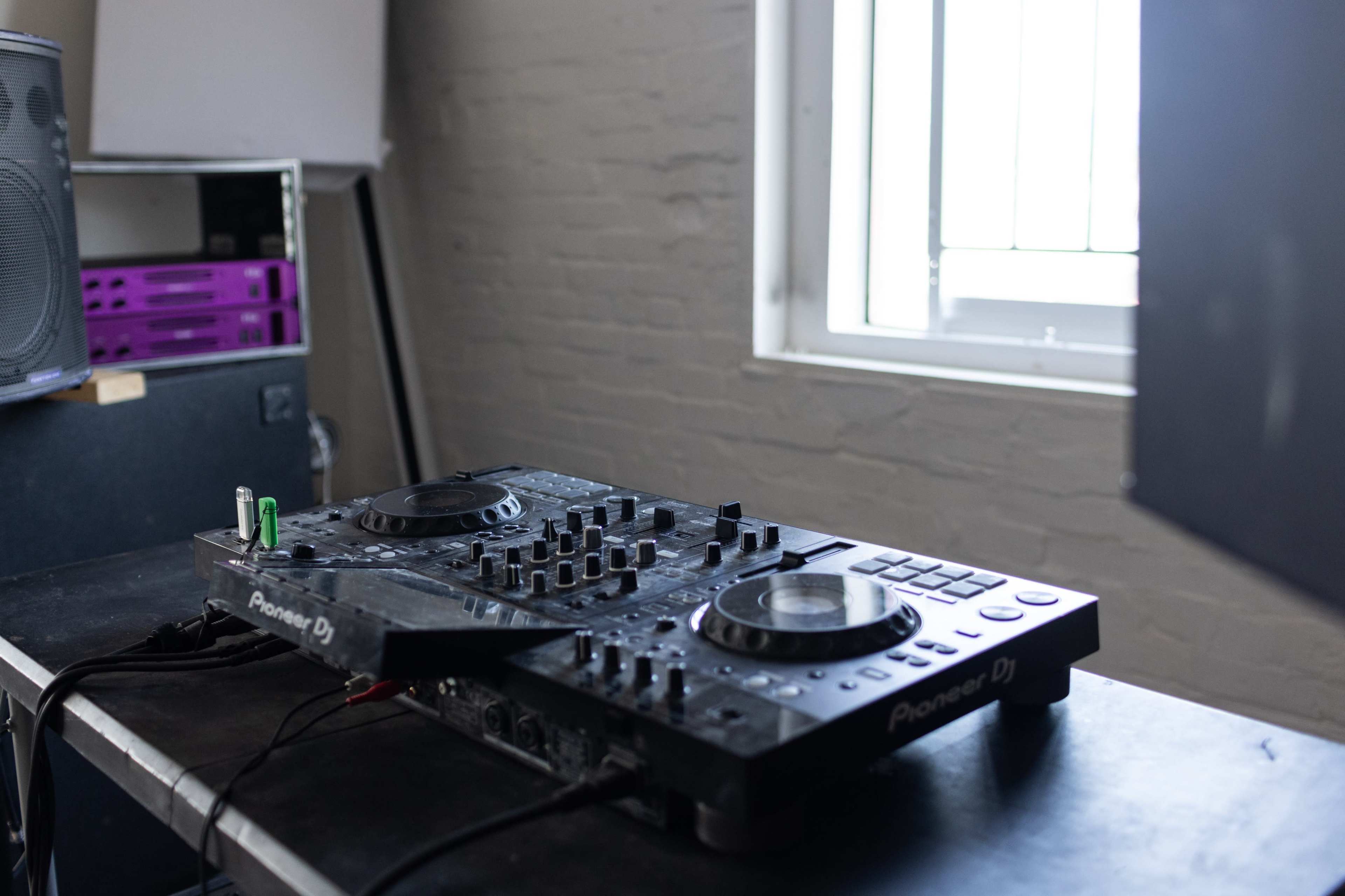 A Pioneer DJ setup is placed on a black table beside a window in a well-lit room.