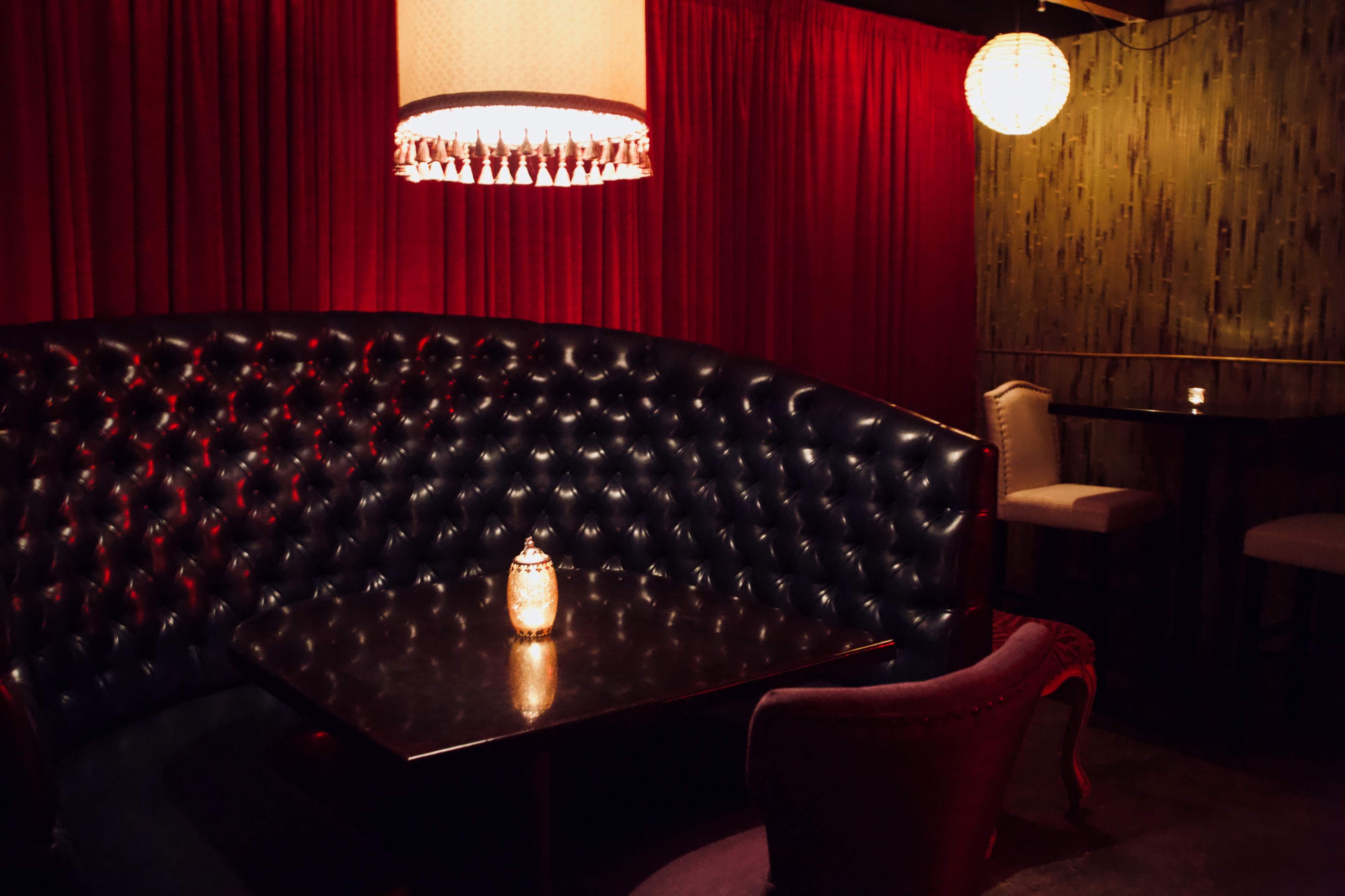 A dimly lit corner booth in a restaurant features plush black seating, a dark table, and ornate lighting fixtures above.