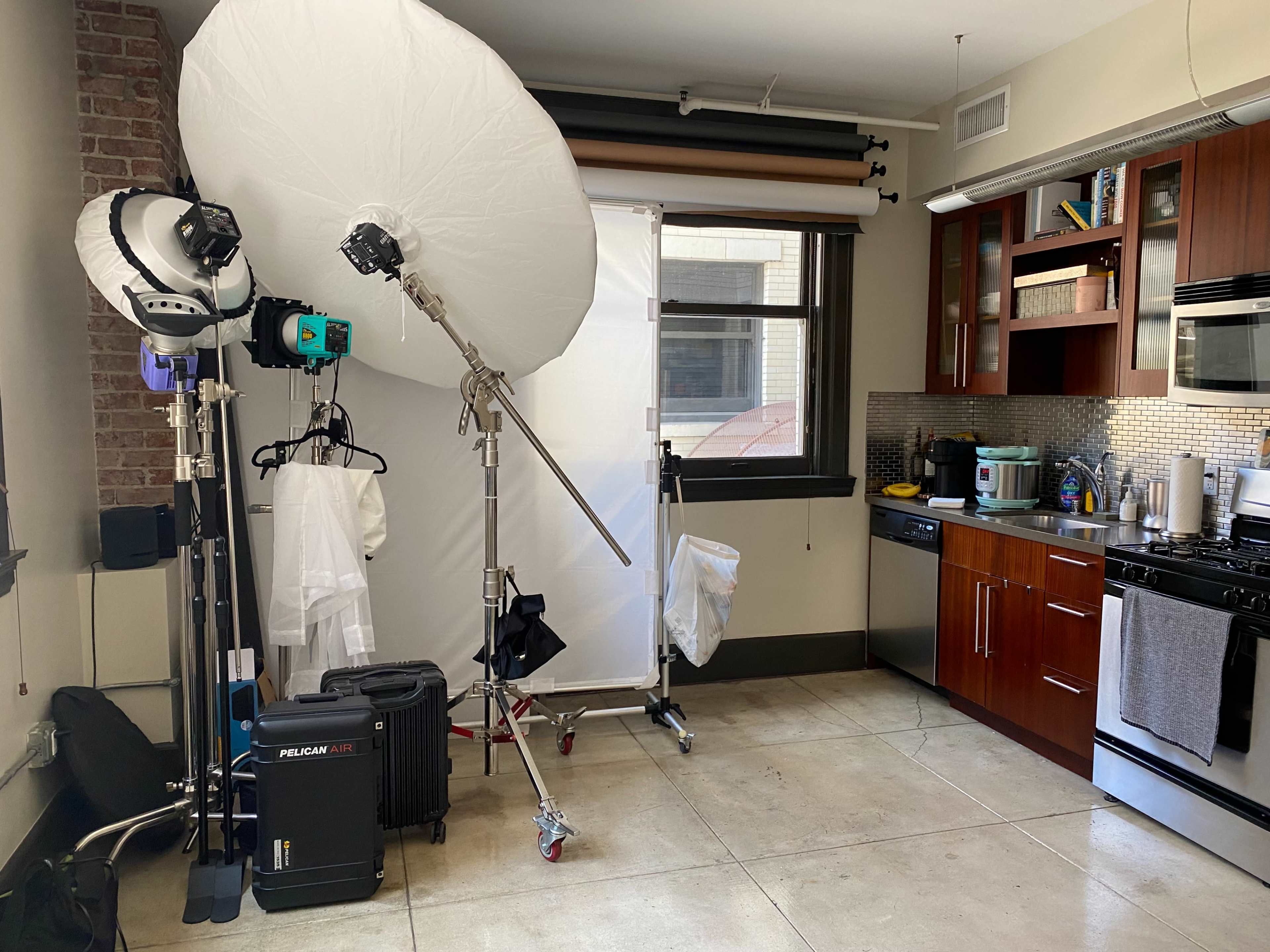 A photography setup with soft lighting equipment and a backdrop is positioned in a modern kitchen space.