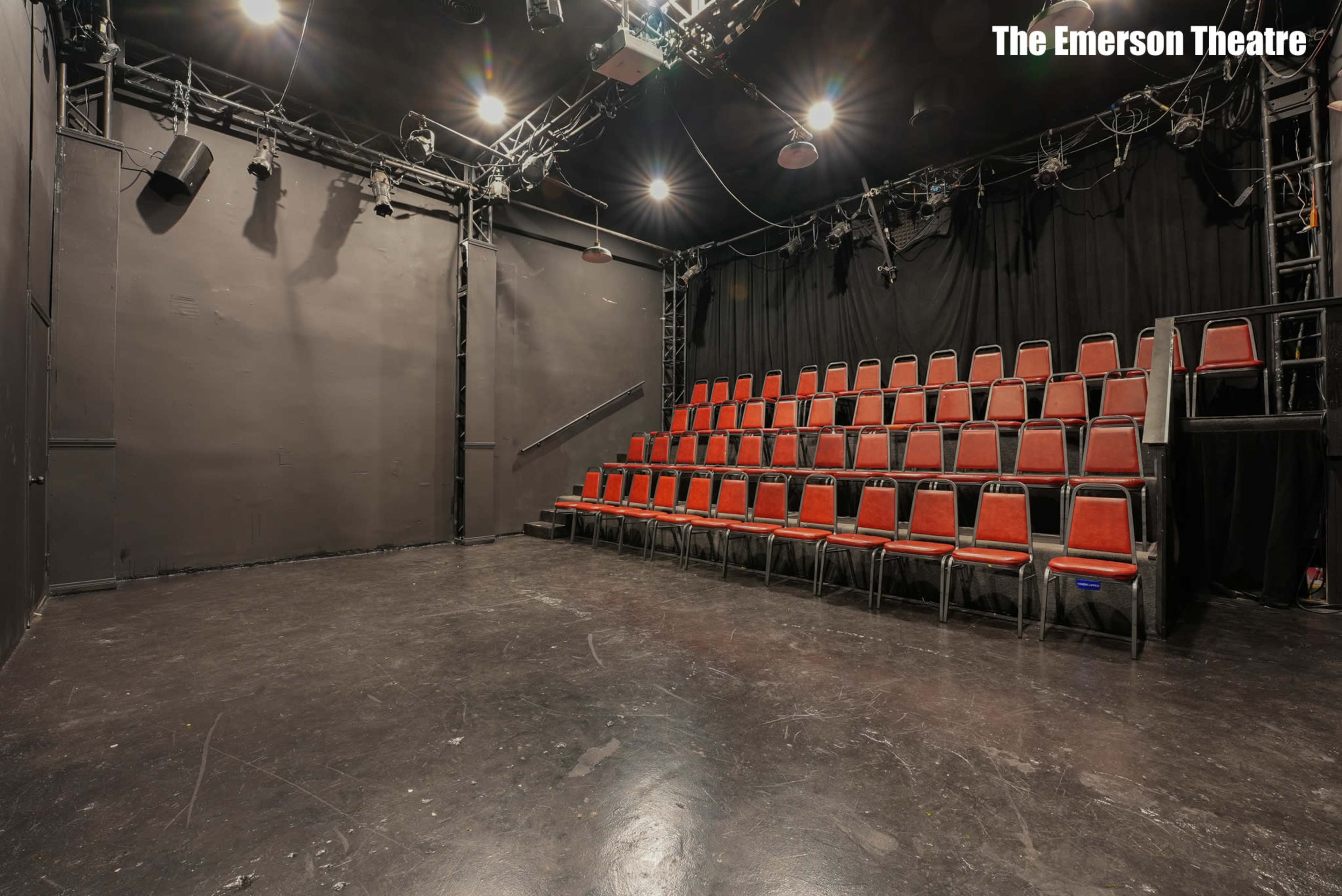The image shows an empty black box theater with red-stacked seating arranged against the back wall.