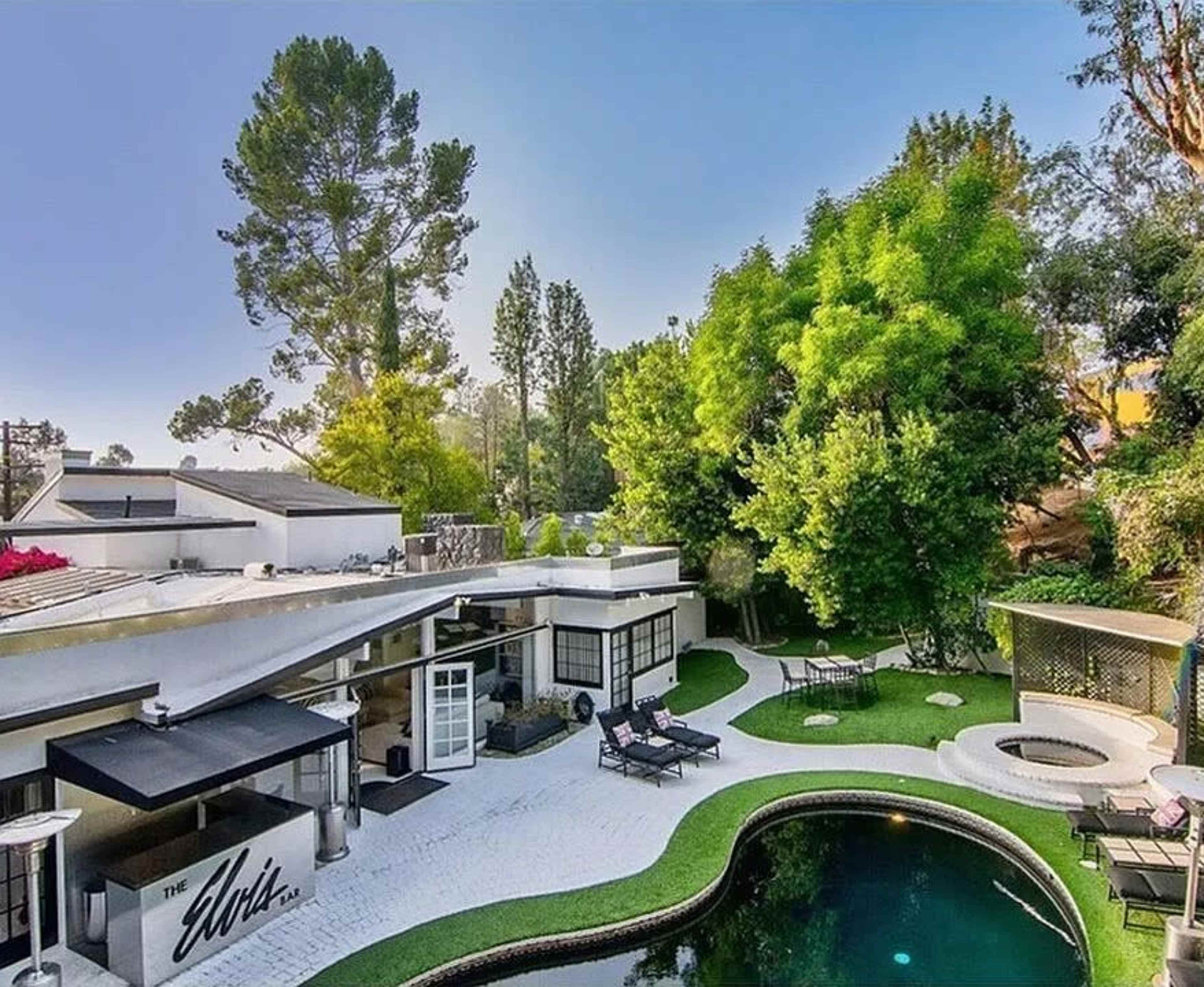 The image shows a modern house with a swimming pool surrounded by landscaped greenery and lounge chairs.